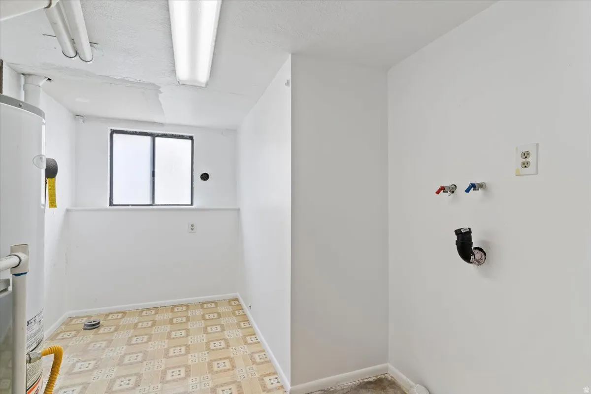 Laundry area with light floors, gas water heater, a textured ceiling, and washer hookup