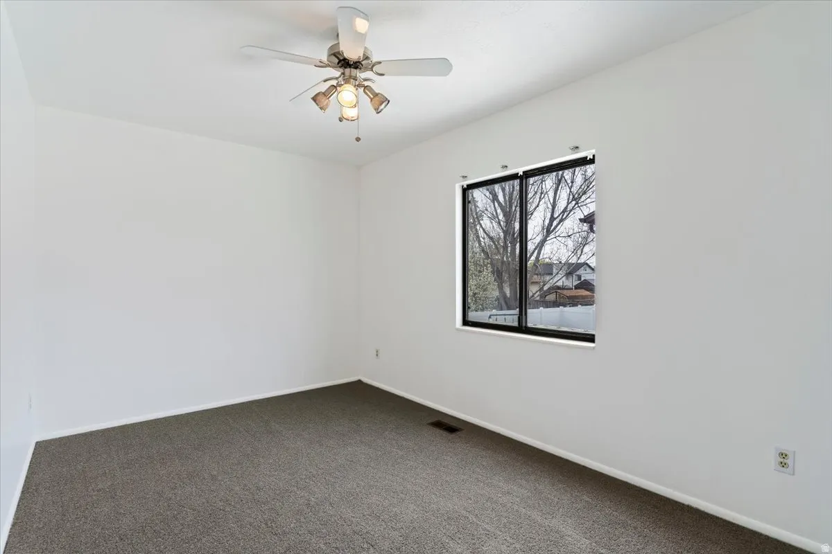Unfurnished room featuring ceiling fan and dark carpet