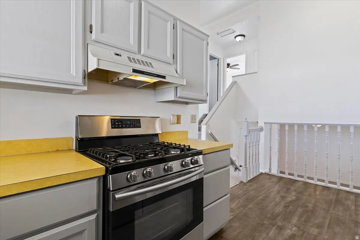 Kitchen with stainless steel gas range oven, gray cabinetry, light countertops, and dark wood-type flooring