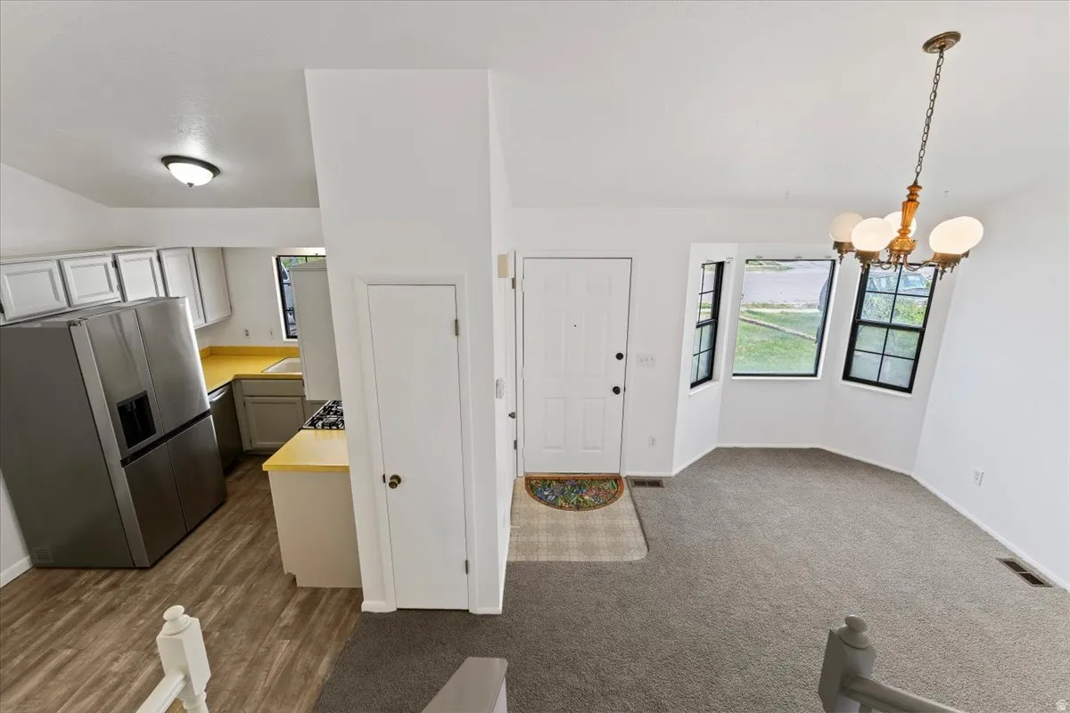 Kitchen featuring stainless steel refrigerator with ice dispenser, light countertops, white cabinetry, and suspended lighting