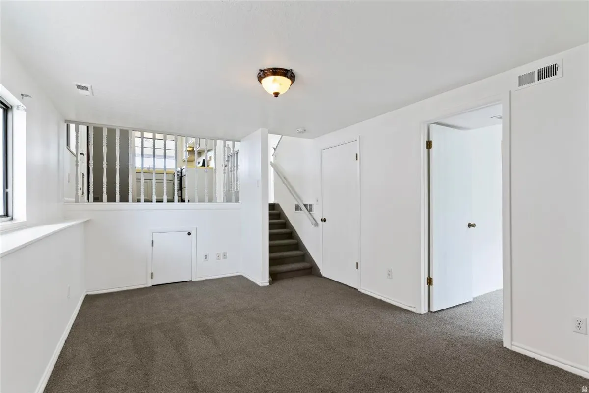 Empty room featuring stairway and dark colored carpet