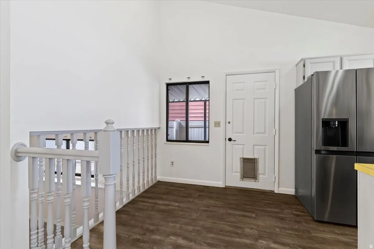 Kitchen with stainless steel refrigerator with ice dispenser, dark wood-style flooring, white cabinetry, lofted ceiling, and light countertops