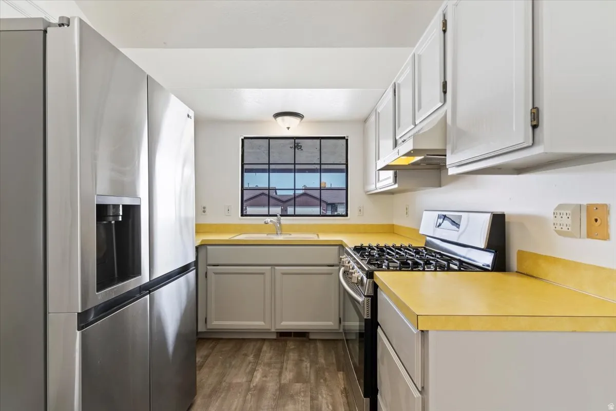 Kitchen featuring stainless steel appliances, dark wood-style flooring, light countertops, and gray cabinetry