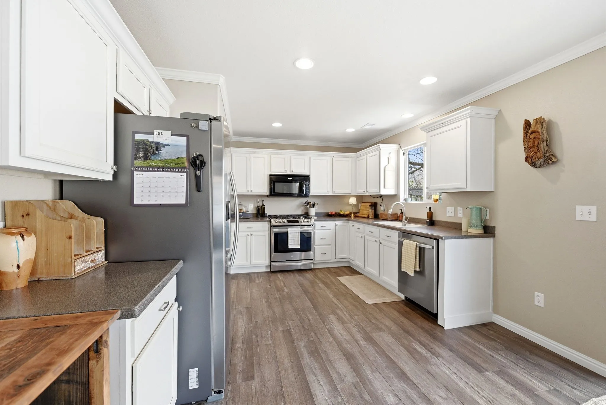 Kitchen featuring dark countertops, stainless steel appliances, white cabinetry, light wood-style flooring, and crown molding
