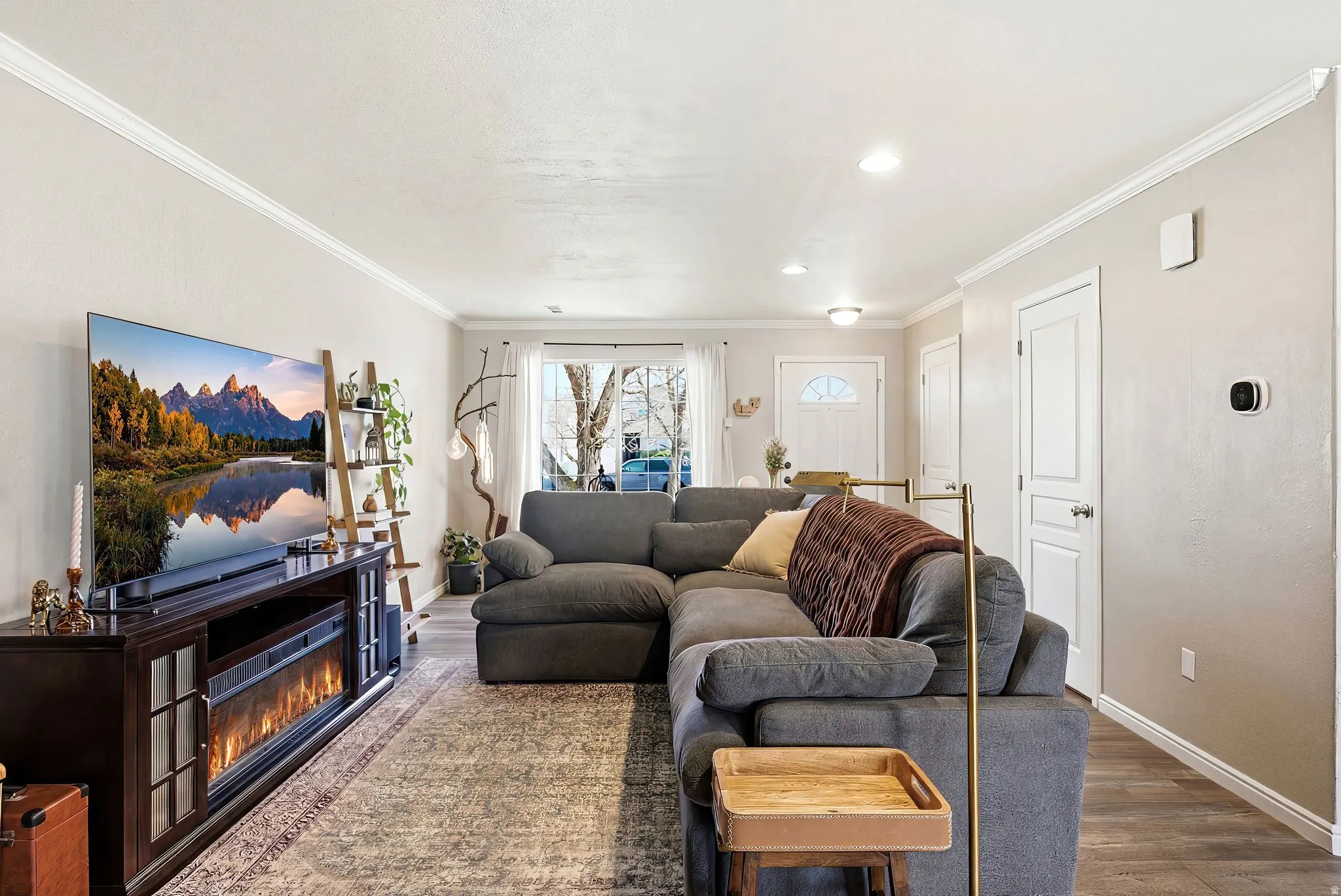 Living room with wood finished floors, a glass covered fireplace, and ornamental molding