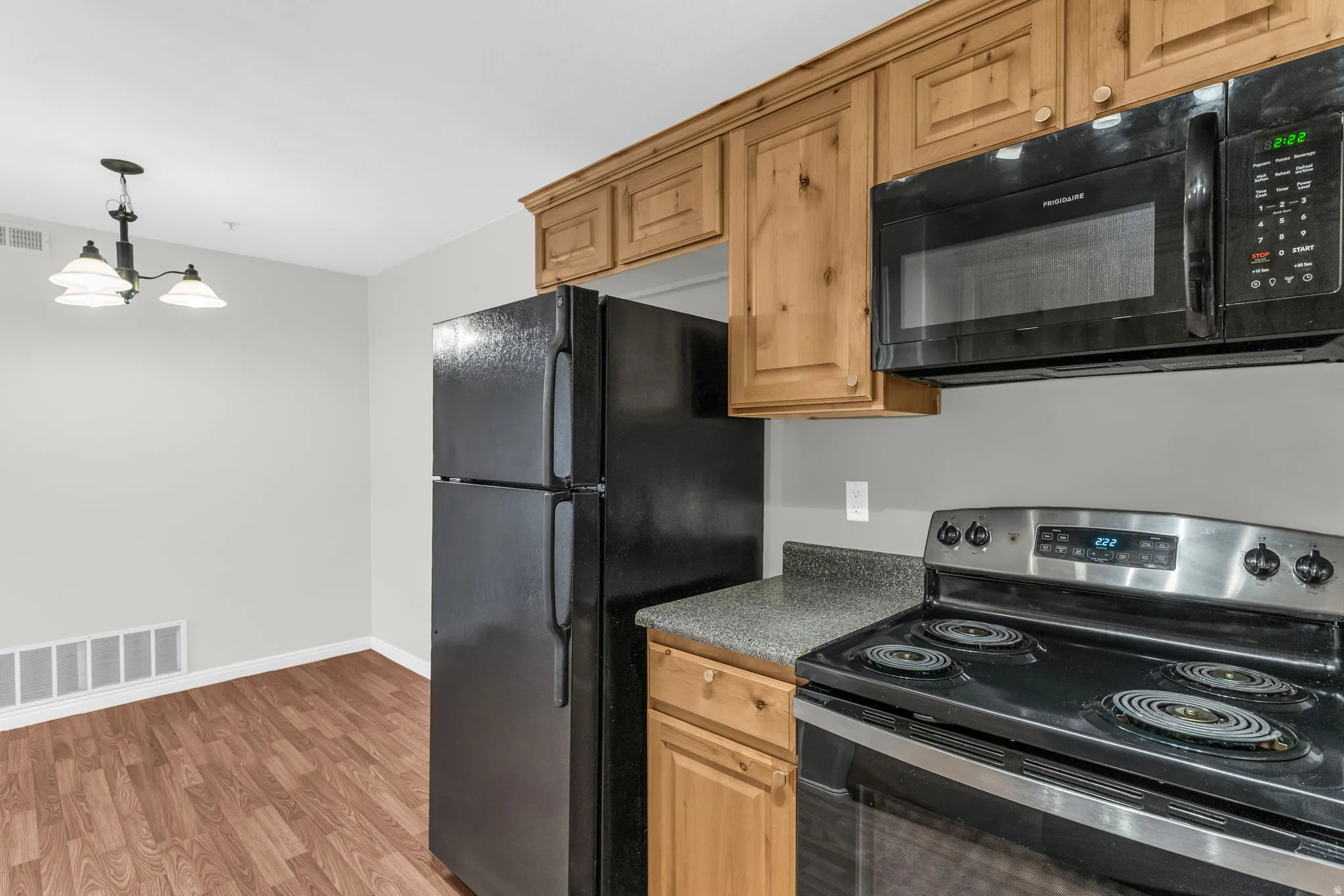 Kitchen with black appliances, dark countertops, light wood-type flooring, and a chandelier