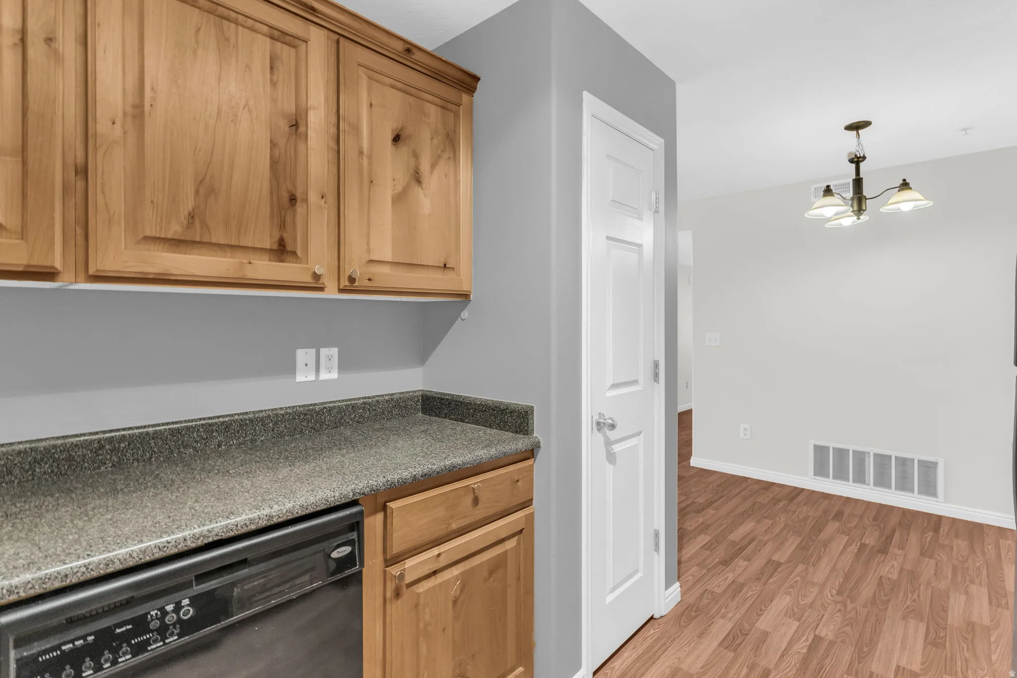 Kitchen featuring dark countertops, black dishwasher, light wood-style flooring, and hanging lights