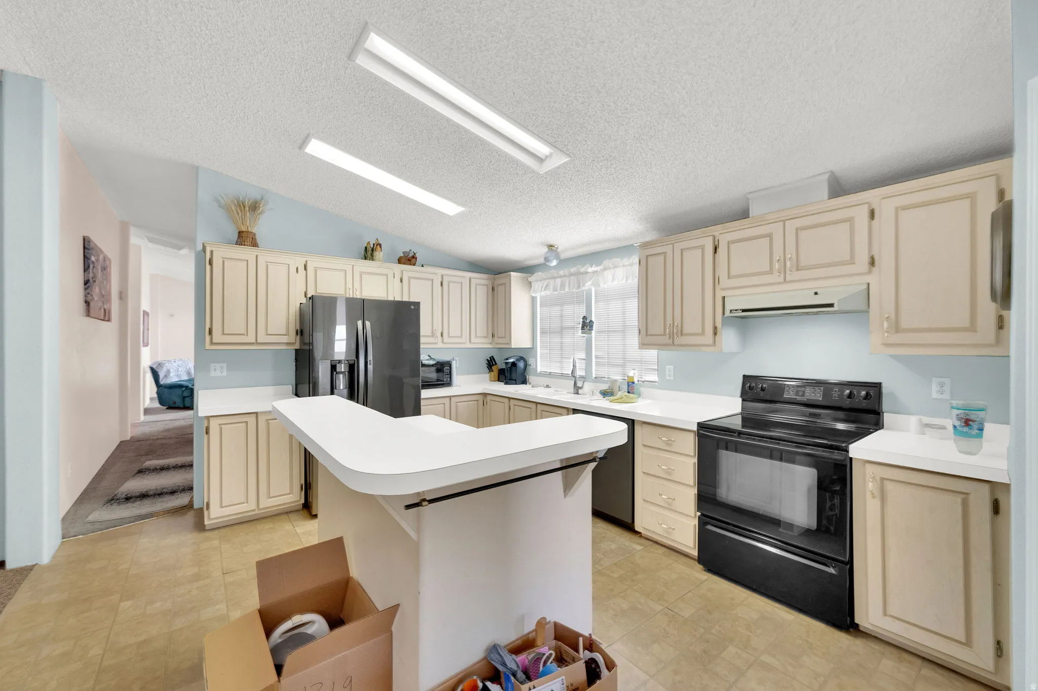 Kitchen with cream cabinets, black appliances, light countertops, and a kitchen island
