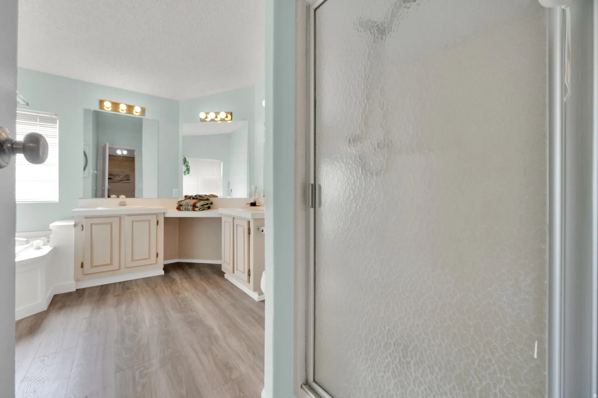 Bathroom featuring vanity, light wood-style floors, a stall shower, a textured ceiling, and a bath in primary bath