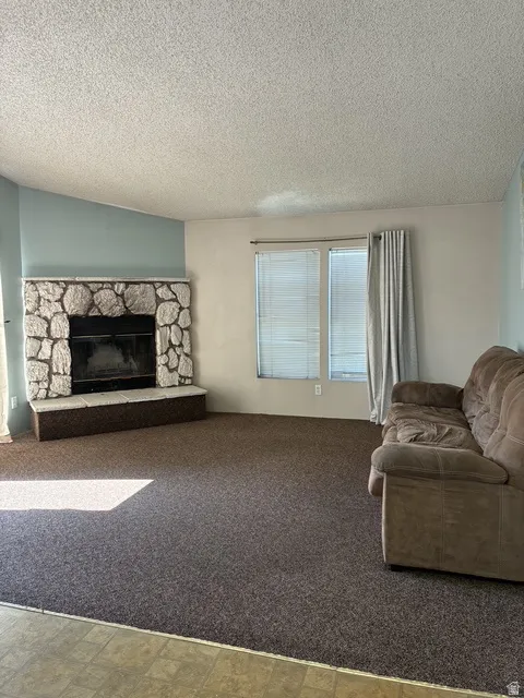 Stone-clad fireplace with a raised hearth, large window, and carpeted flooring