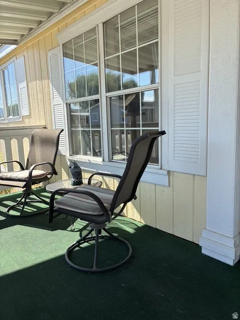 Covered porch with green outdoor carpeting, white window frames, and horizontal siding