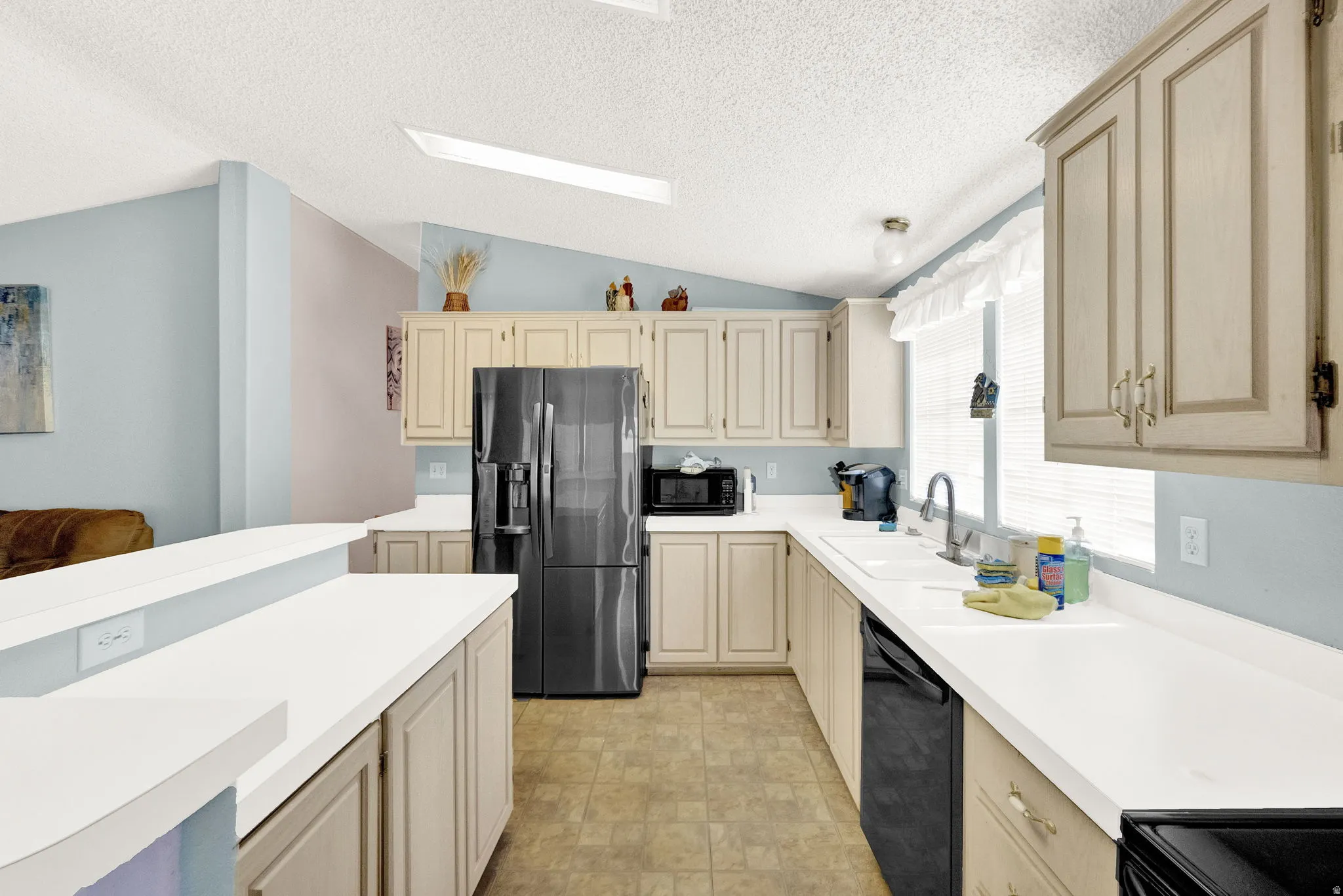 Kitchen with black appliances, light countertops, cream cabinetry, and stone finish flooring