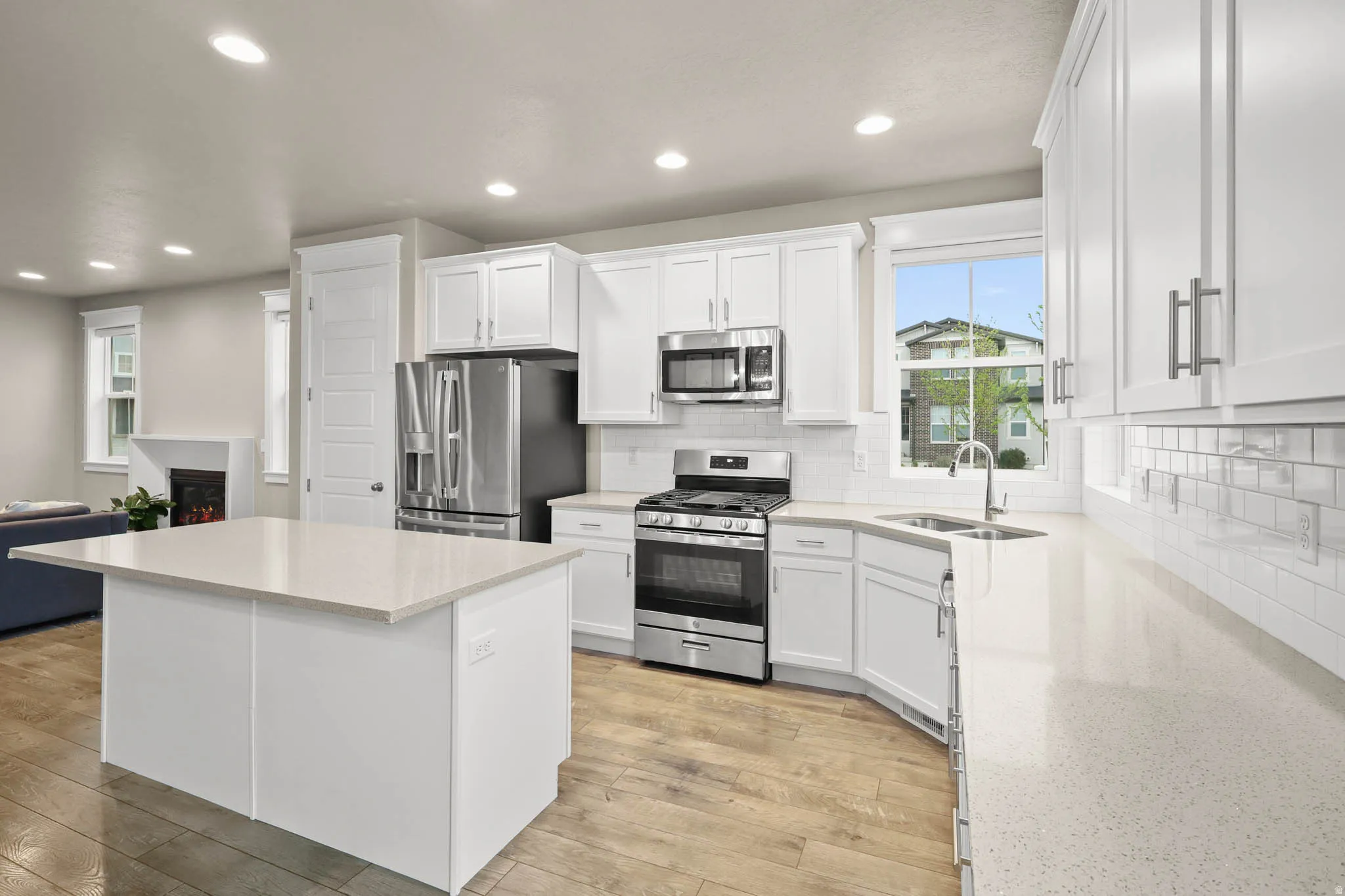 Kitchen featuring white cabinetry, stainless steel appliances, a lit fireplace, a kitchen island, and decorative backsplash