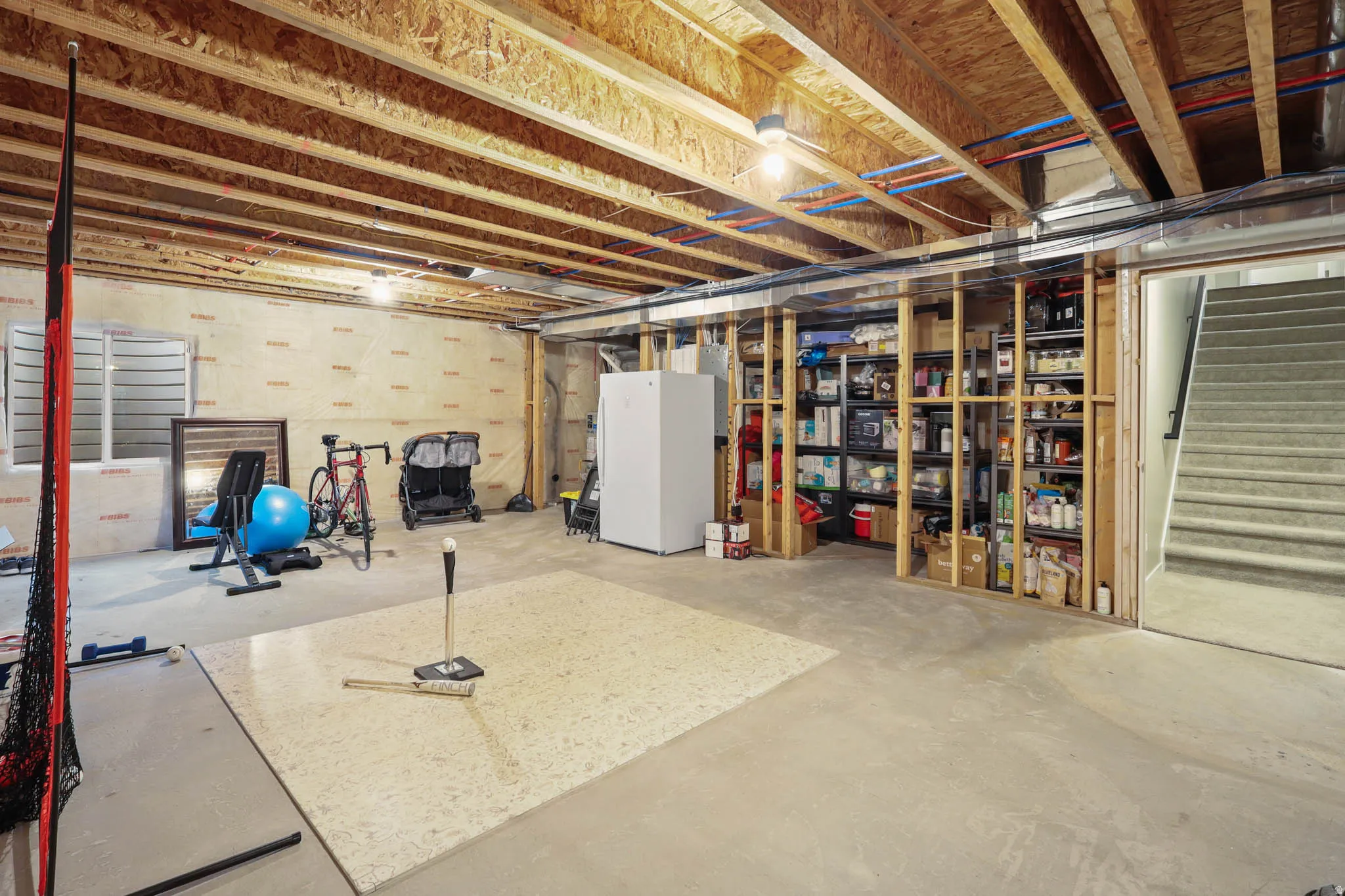 Unfinished basement featuring stairs and freestanding refrigerator