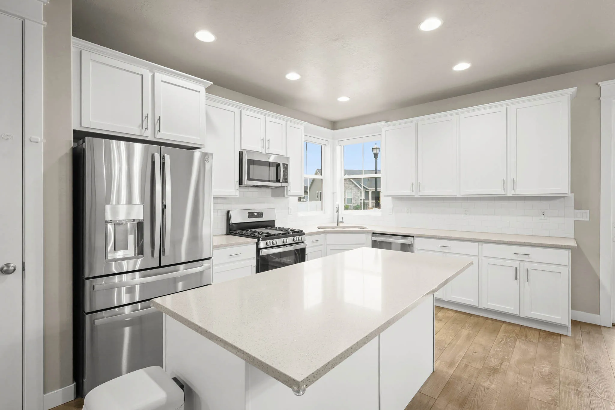 Kitchen featuring stainless steel appliances, white cabinetry, light wood-style flooring, recessed lighting, and a center island