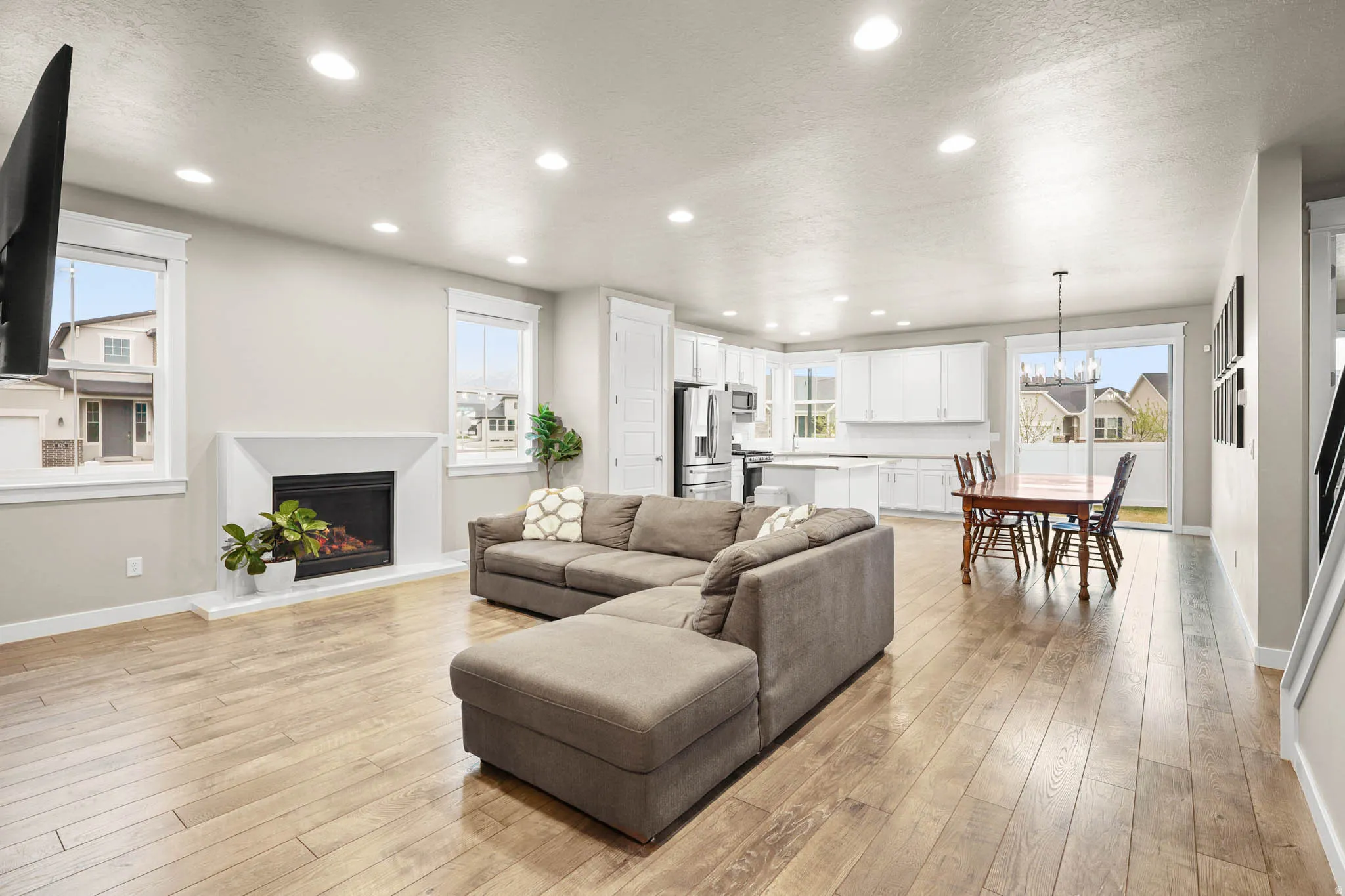 Living room featuring a lit fireplace, light LVP wood-style flooring, a textured ceiling, and suspended lighting