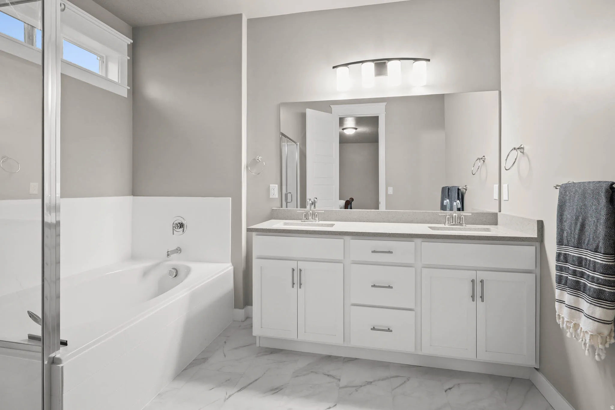 Primary Bathroom featuring a double vanity, a garden tub, a stall shower, and light marble finish flooring