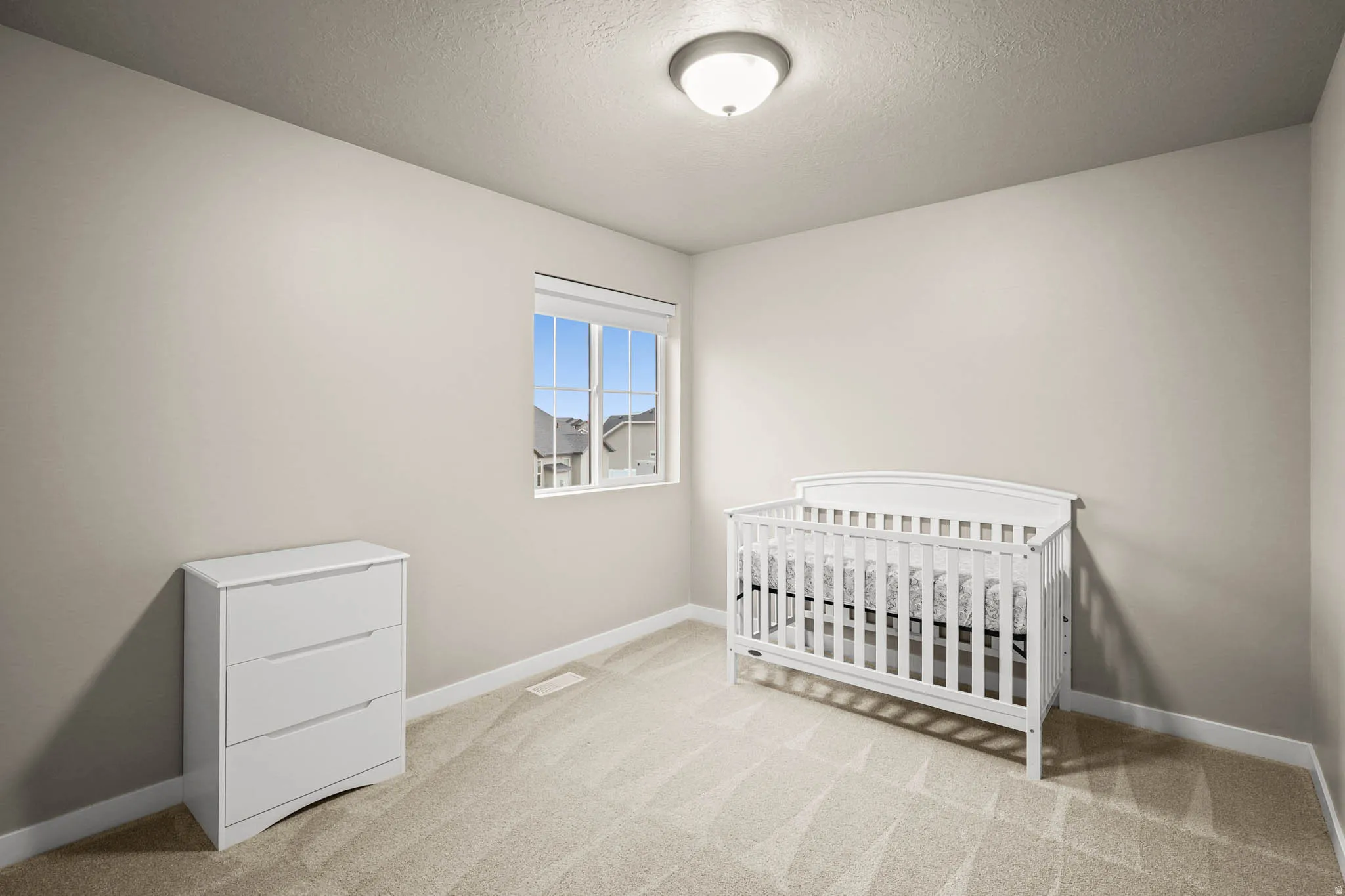 Bedroom featuring a crib, light carpet, and a textured ceiling