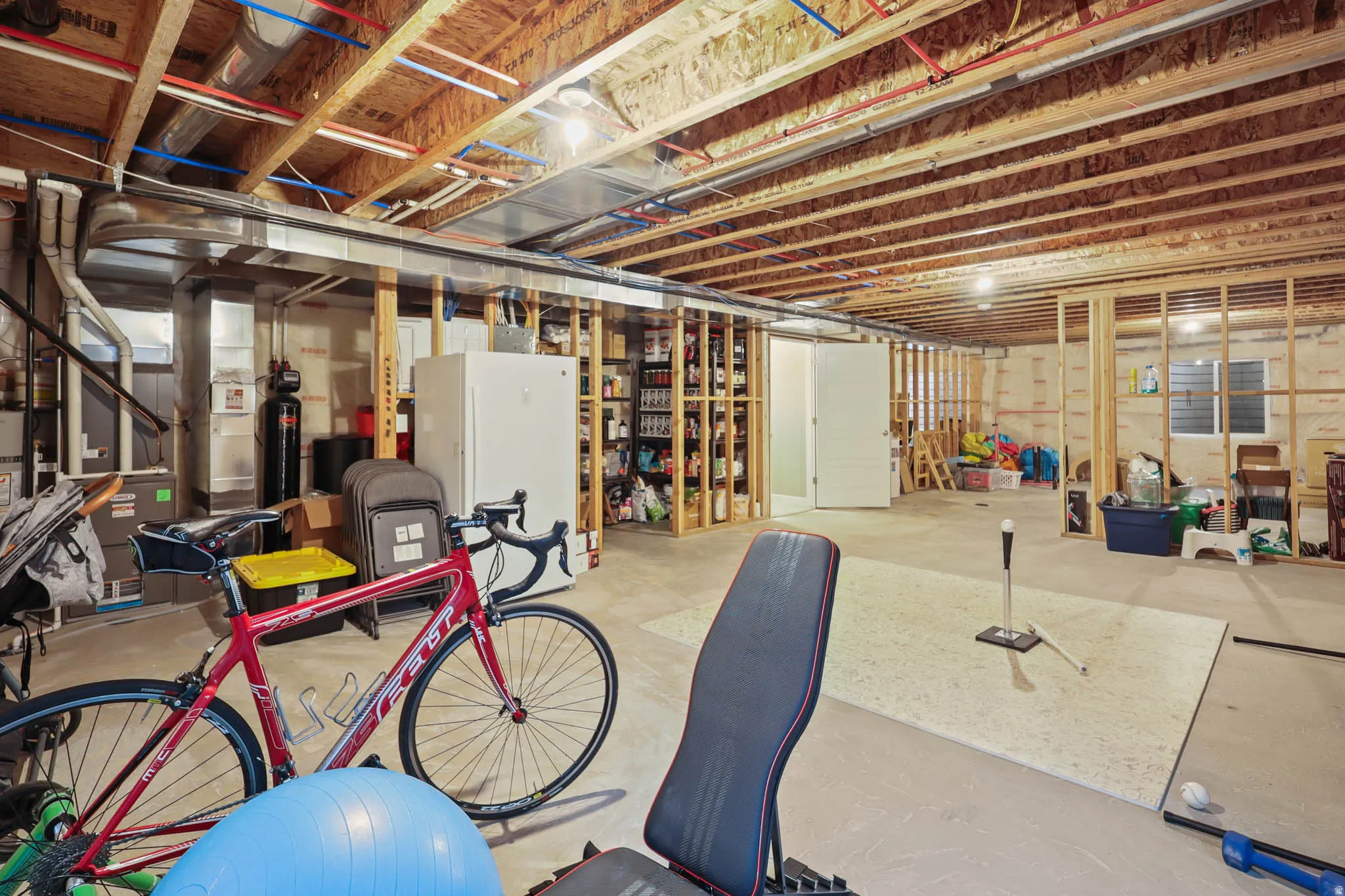 Unfinished basement with freestanding refrigerator and a water softener