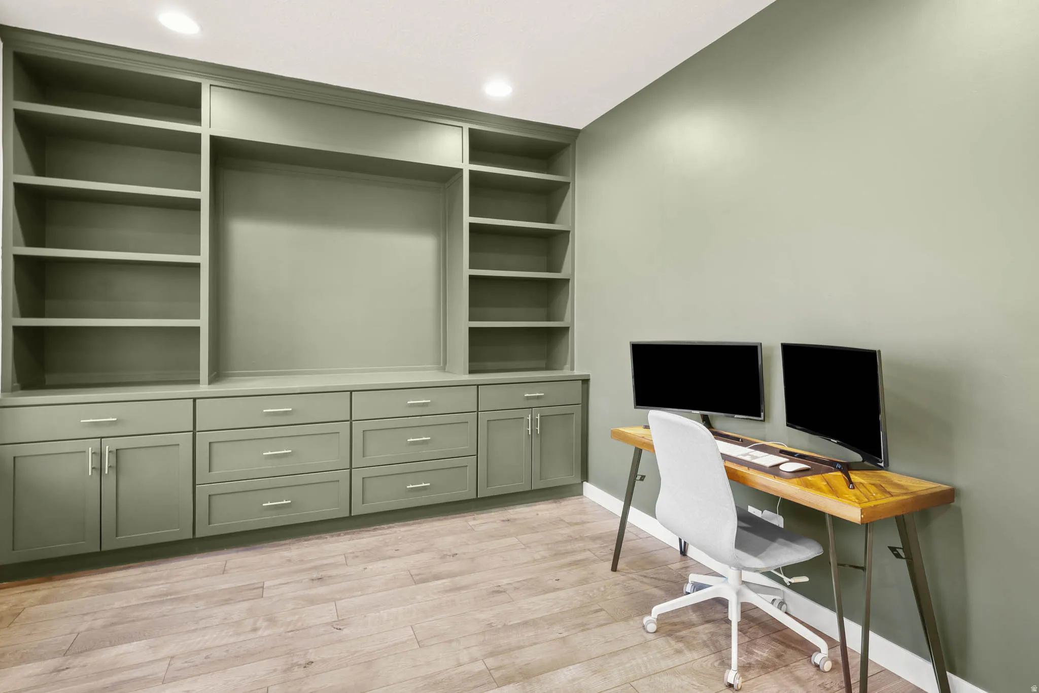 Home office with light wood finished floors, built in shelves, and recessed lighting