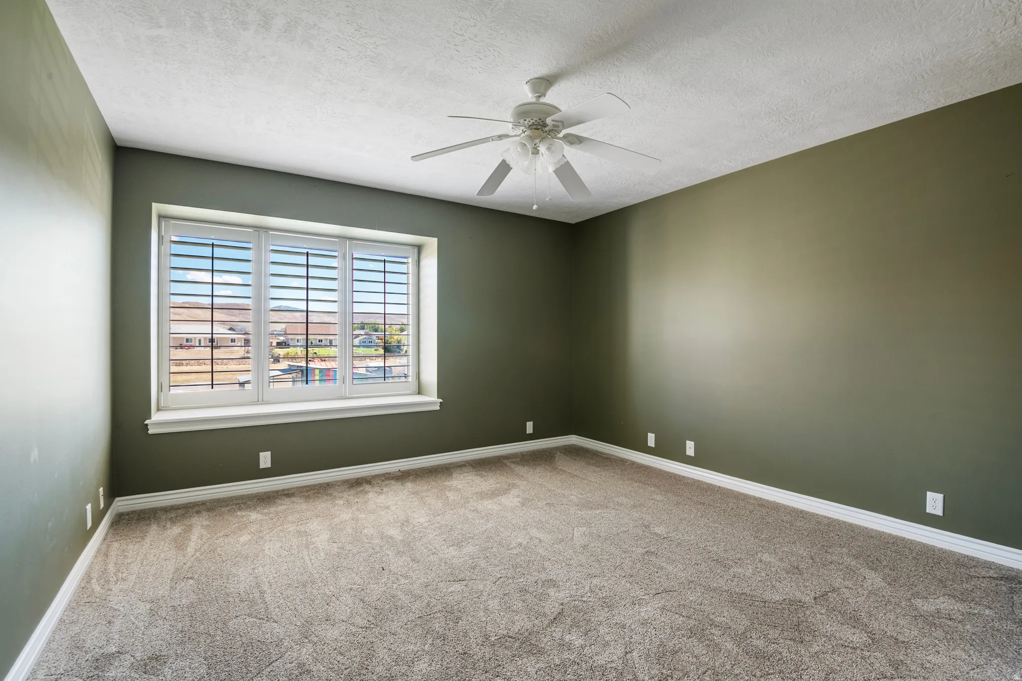 Spare room featuring a ceiling fan, light colored carpet, and a textured ceiling