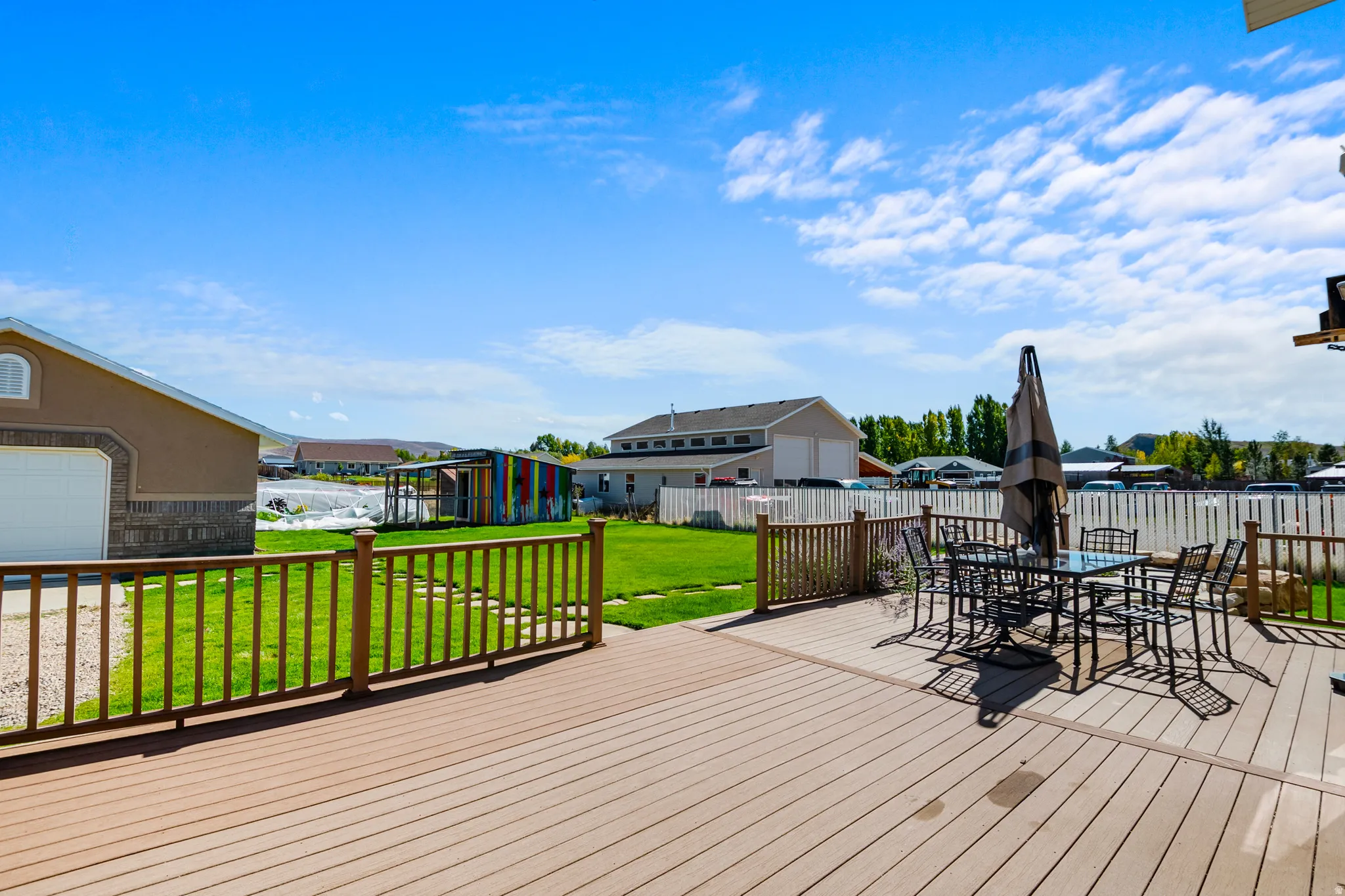 Wooden deck featuring a residential view, outdoor dining space, a fenced backyard, and an outdoor structure