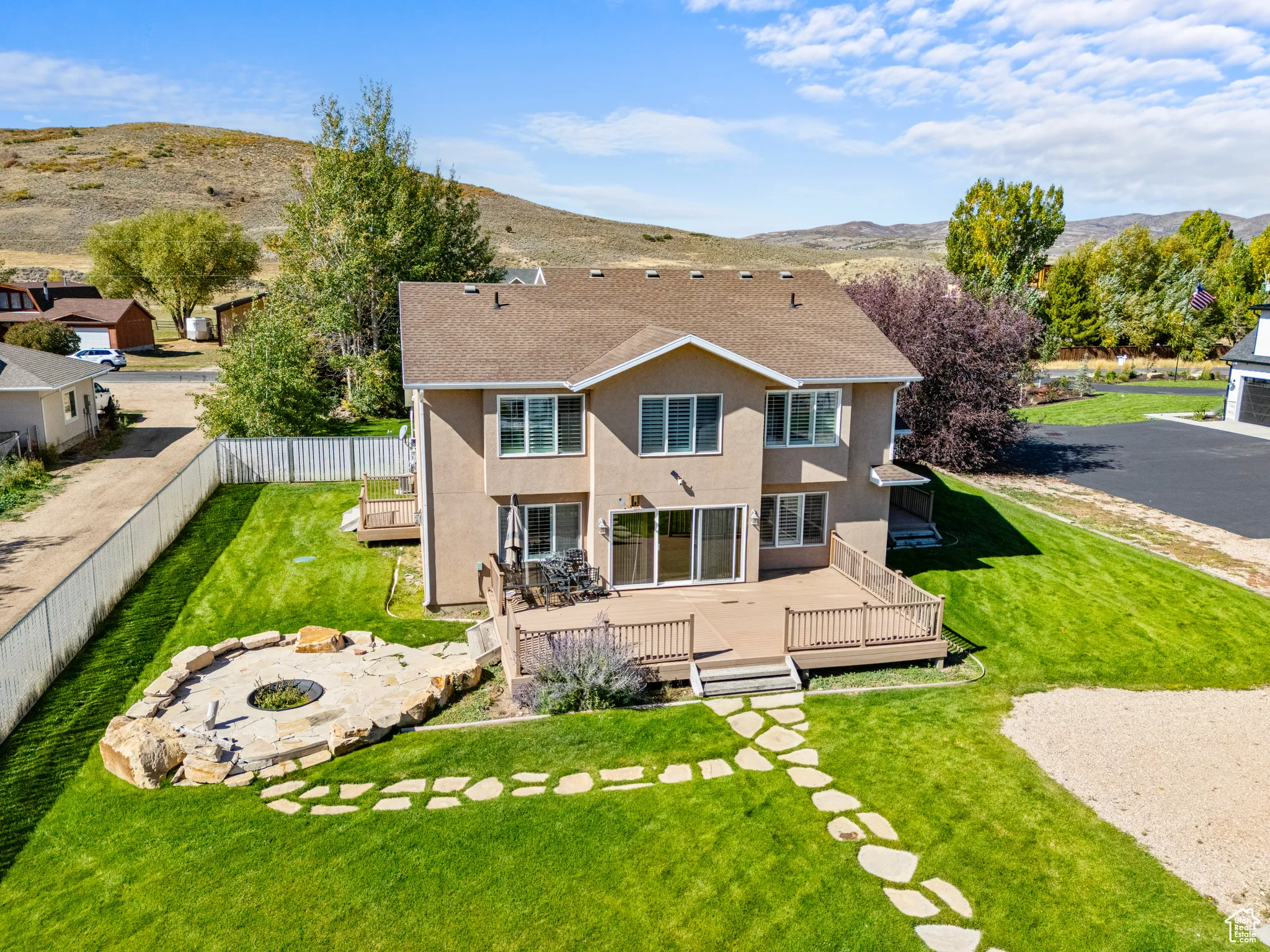 Rear view of property with a fire pit, roof with shingles, a lawn, a deck with mountain view, and stucco siding