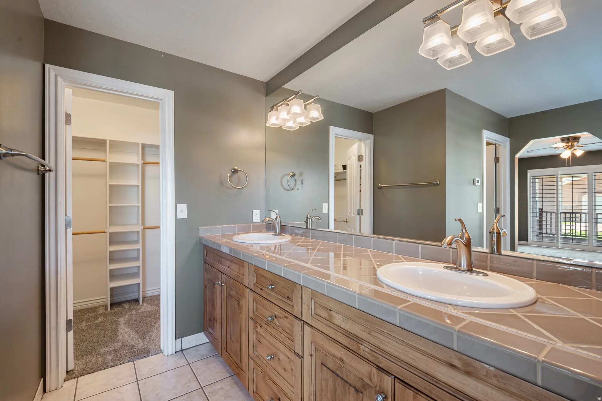 Full bath featuring a walk in closet, double vanity, light tile patterned floors, and ceiling fan