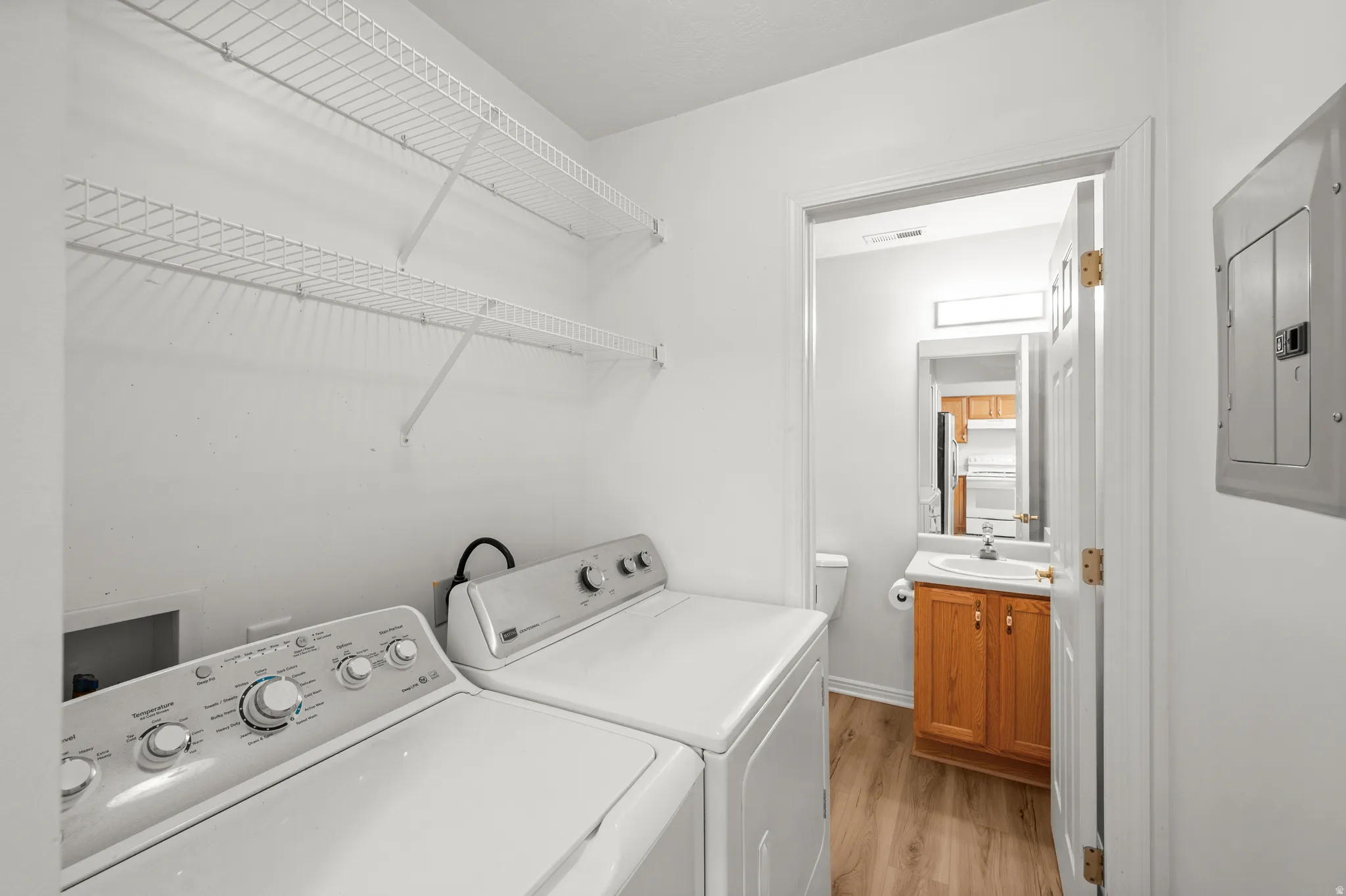Laundry room featuring light wood finished floors, electric panel, and washer and clothes dryer