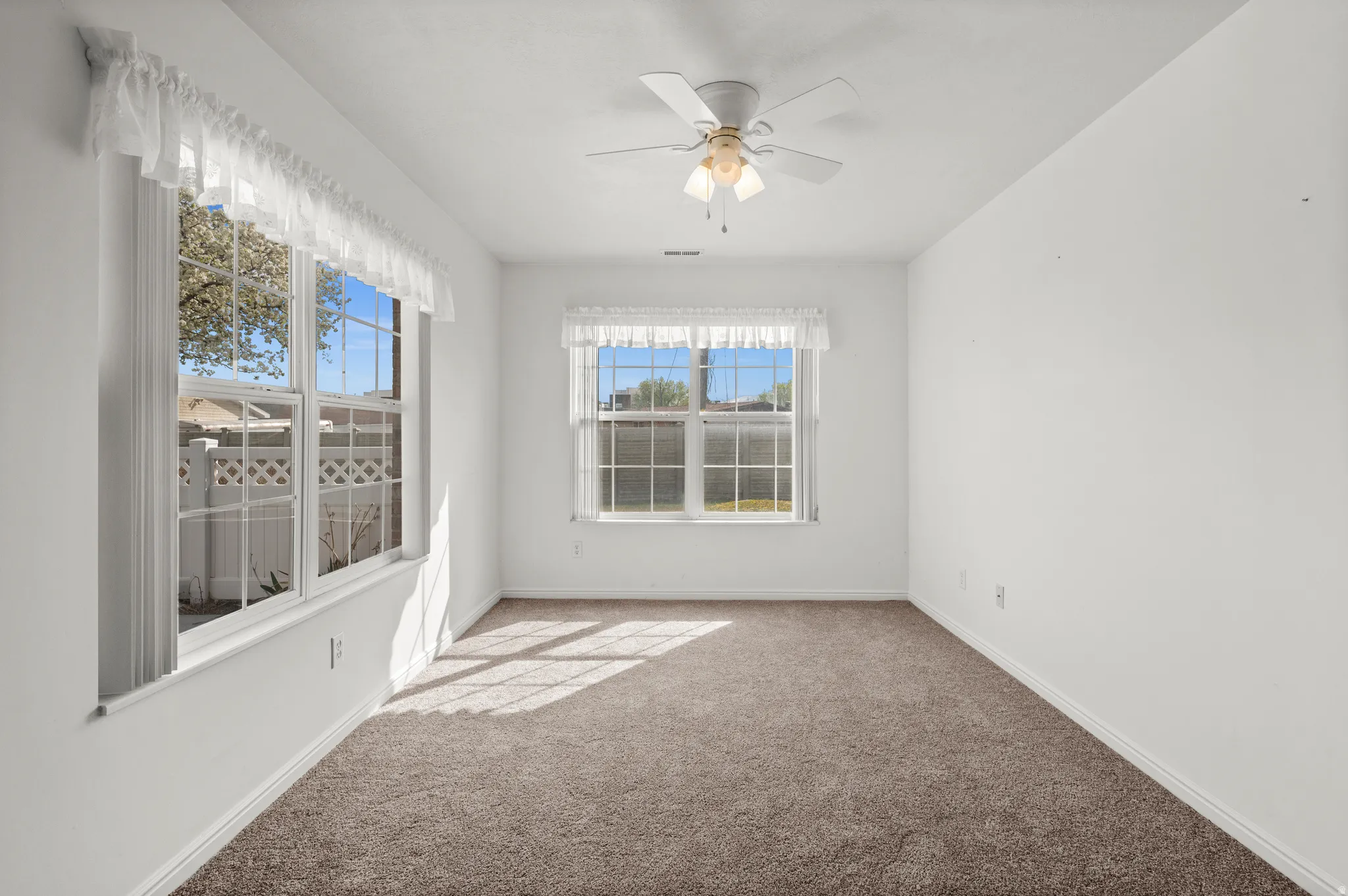 Carpeted spare room with a ceiling fan and plenty of natural light
