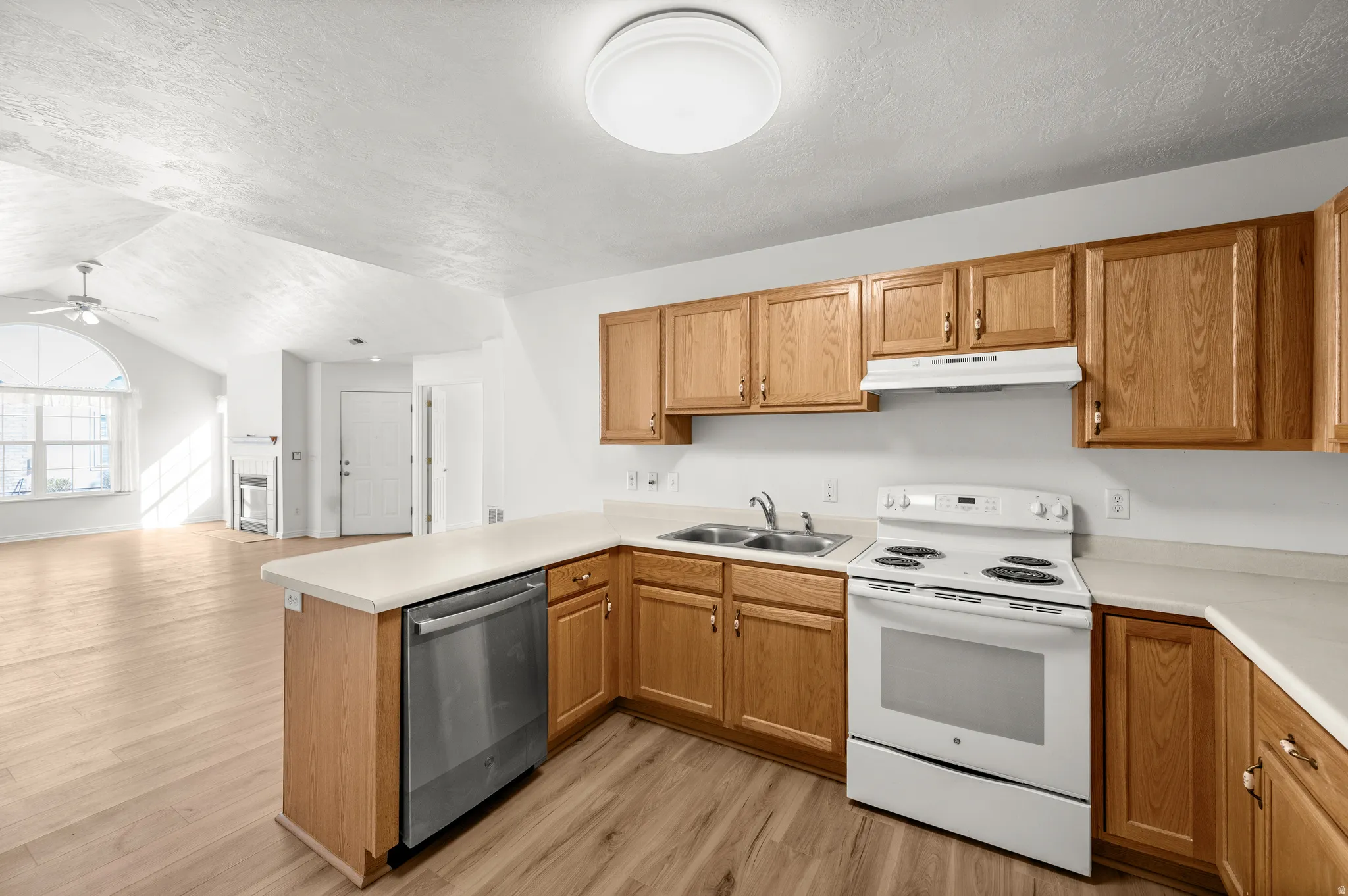 Kitchen with electric stove, light countertops, light wood-type flooring, and dishwasher