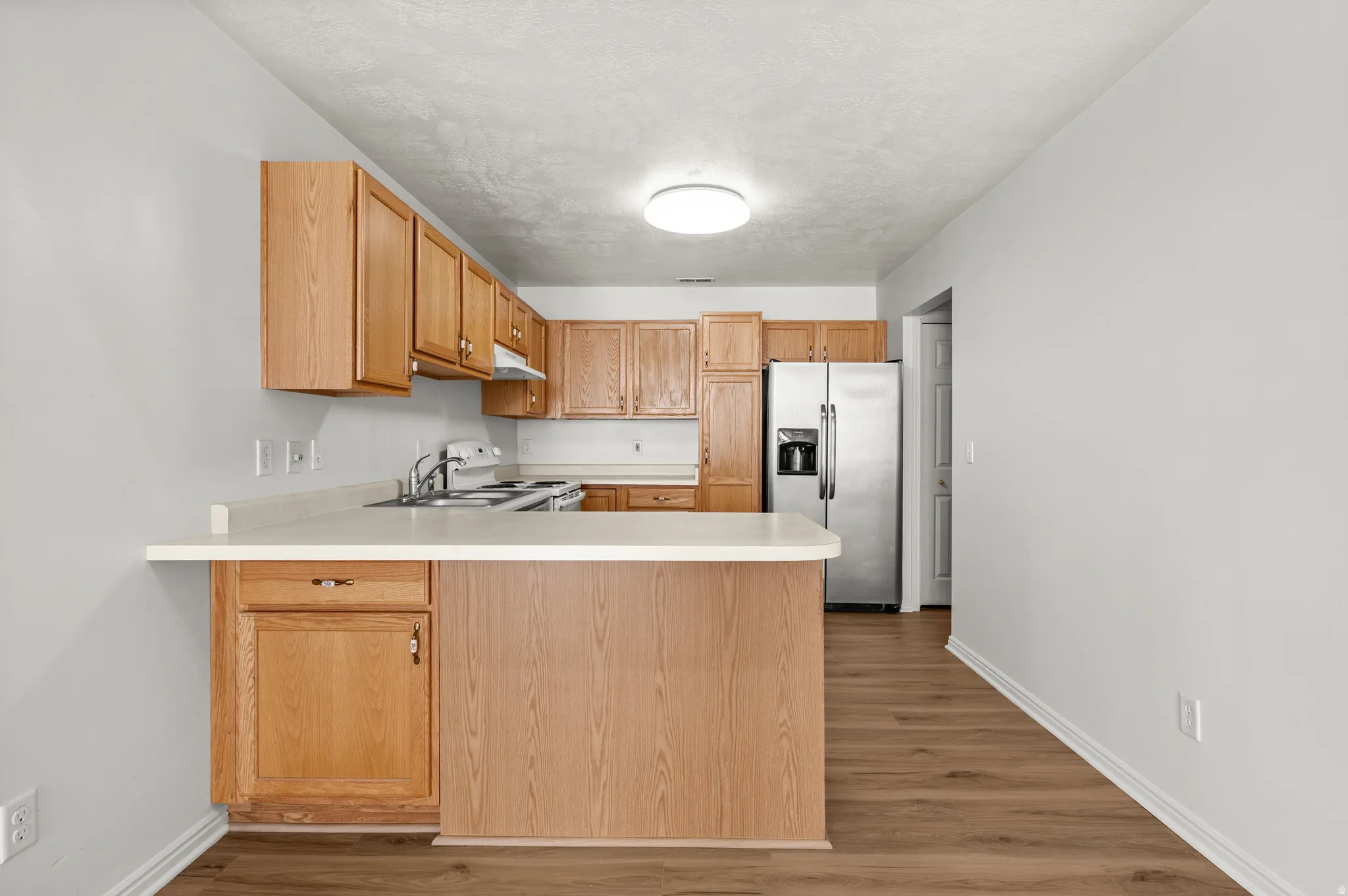 Kitchen featuring light countertops, stainless steel refrigerator with ice dispenser, a peninsula, dark wood finished floors, and electric stove