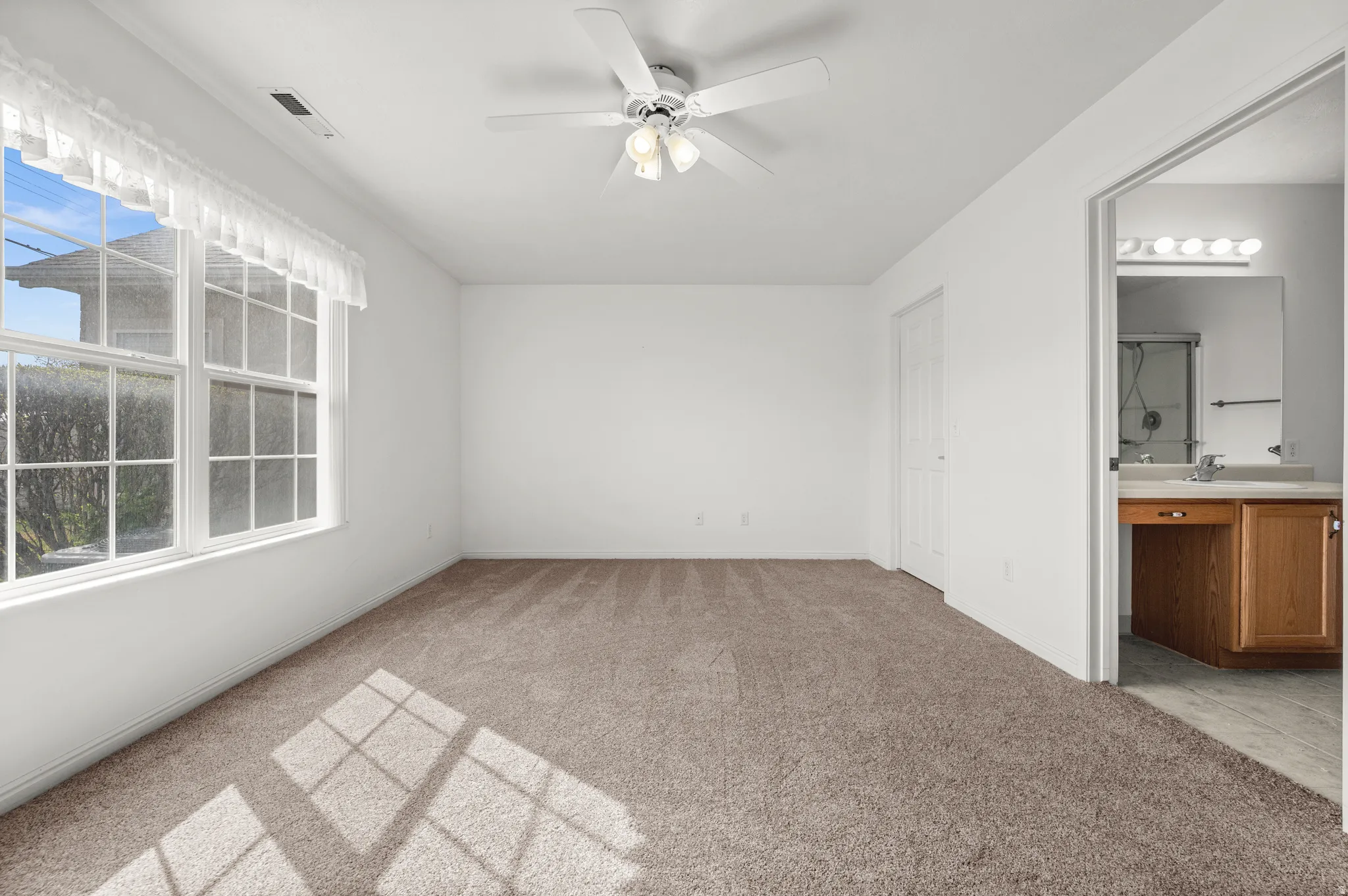 Unfurnished bedroom featuring light carpet, ceiling fan, and ensuite bathroom