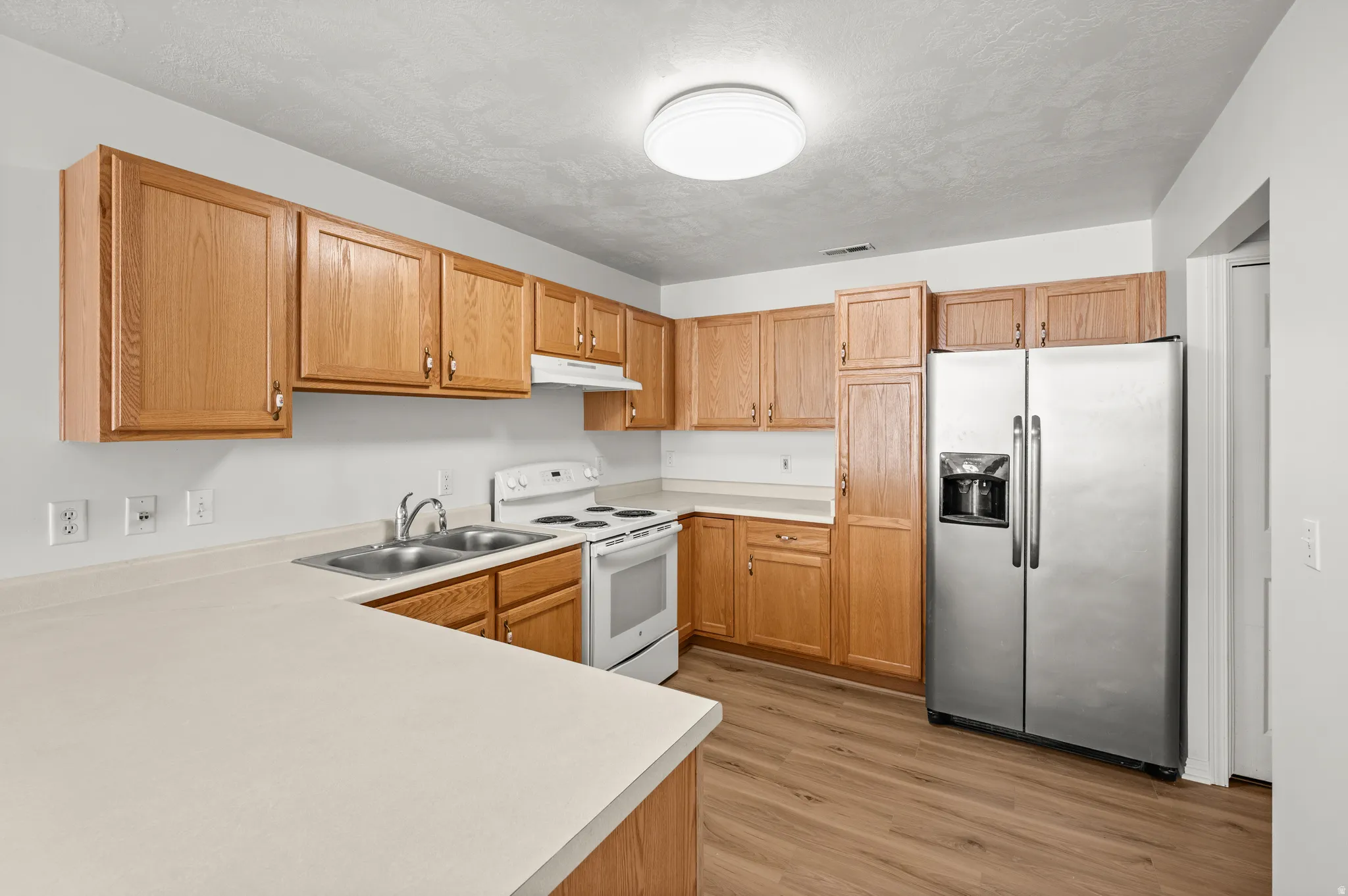 Kitchen featuring stainless steel refrigerator with ice dispenser, white electric range oven, light countertops, light wood-type flooring, and a textured ceiling