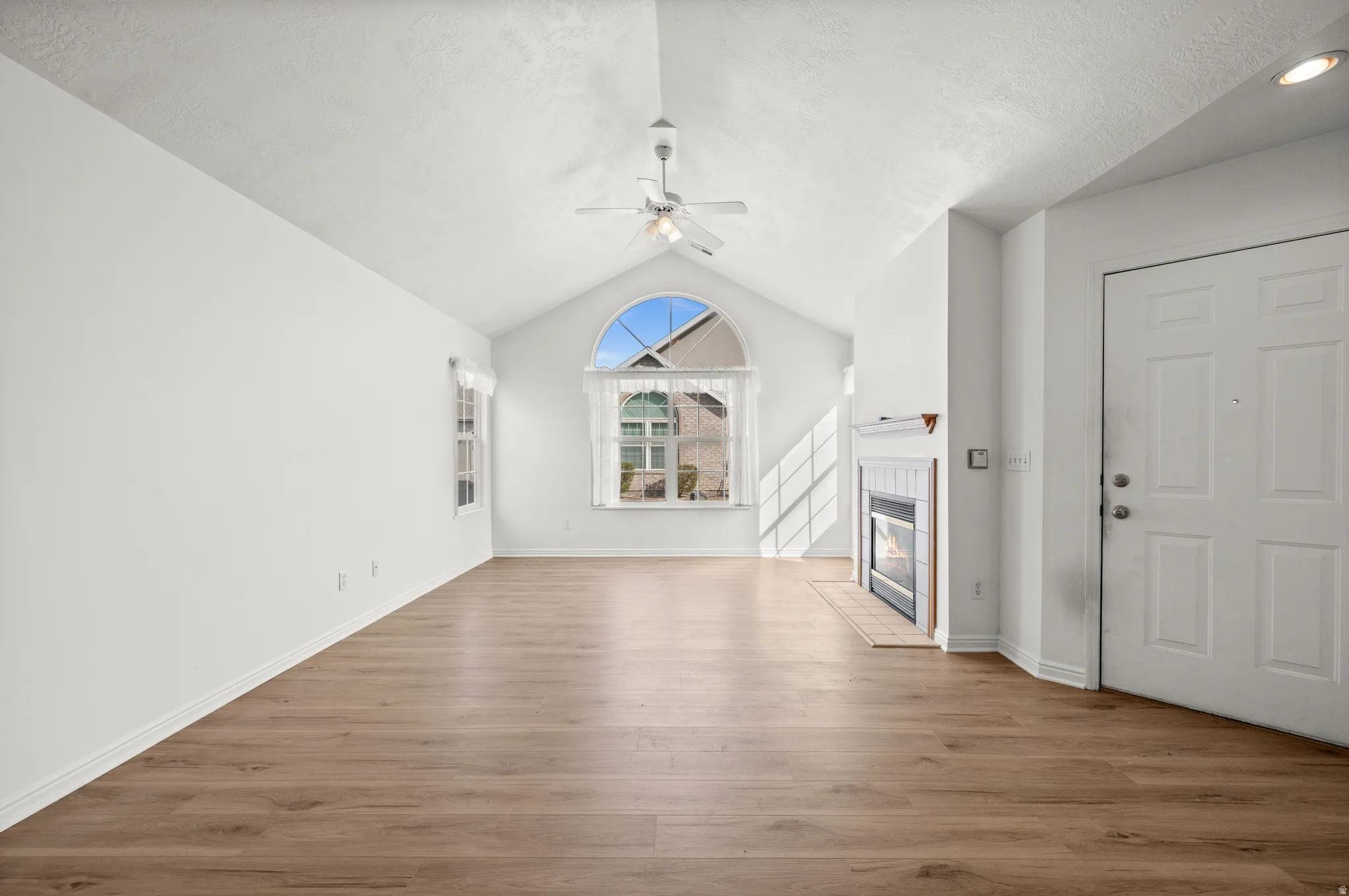 Unfurnished living room featuring ceiling fan, a tile fireplace, light wood finished floors, and a textured ceiling