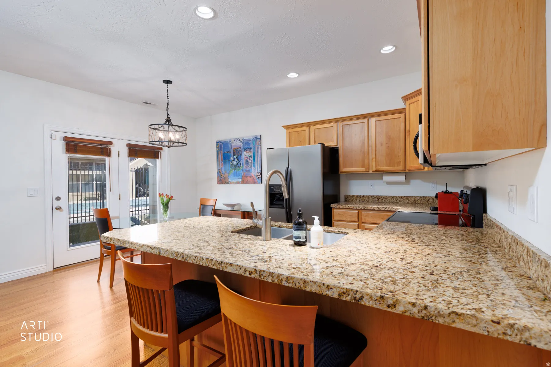 Kitchen with a peninsula, light stone countertops, stainless steel fridge with ice dispenser, black stove, and a kitchen breakfast bar