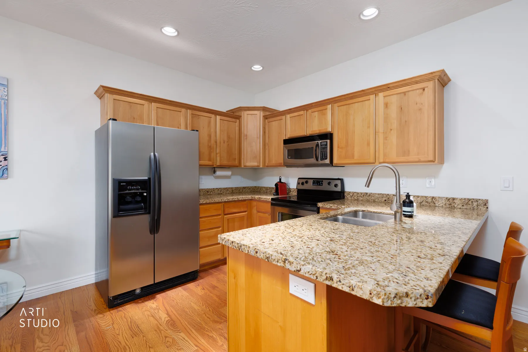 Kitchen featuring light stone countertops, stainless steel appliances, a peninsula, light wood-style flooring, and a kitchen breakfast bar