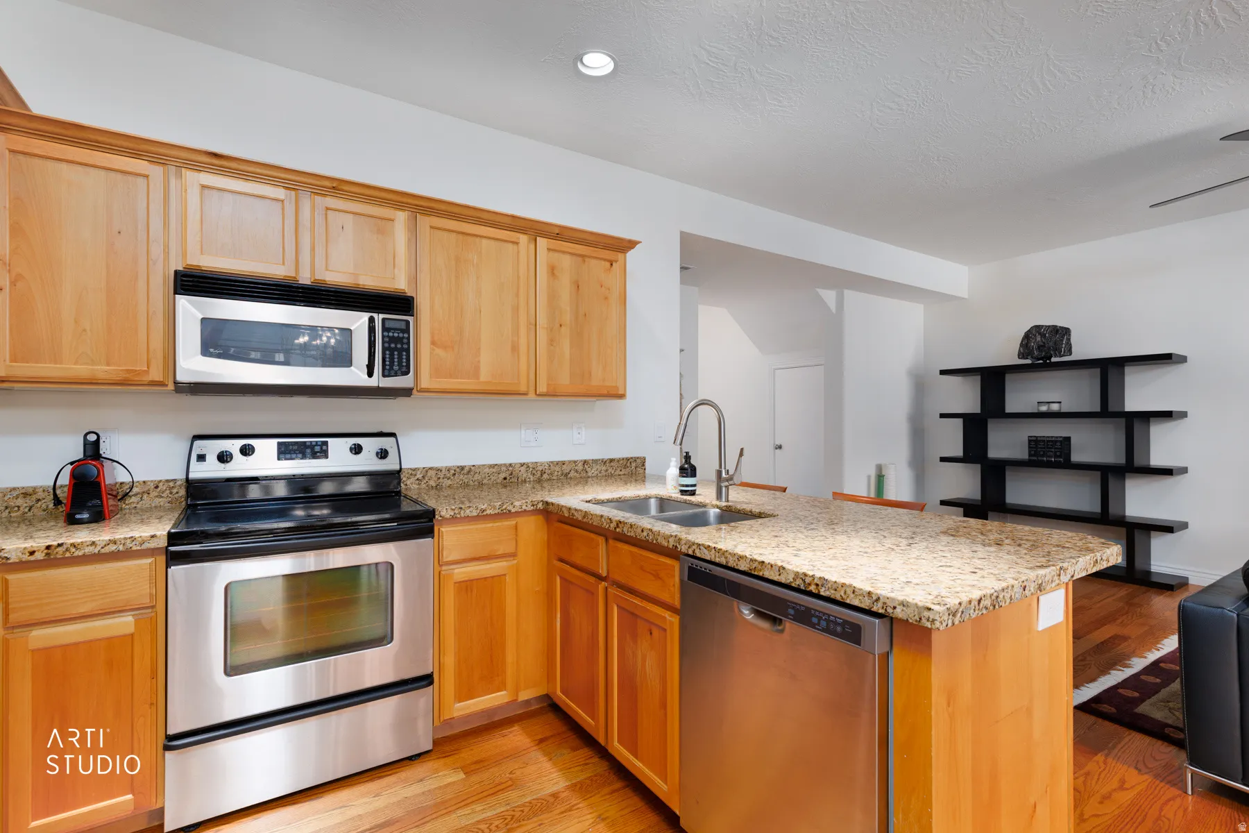 Kitchen with stainless steel appliances, a peninsula, light stone countertops, and light wood-type flooring