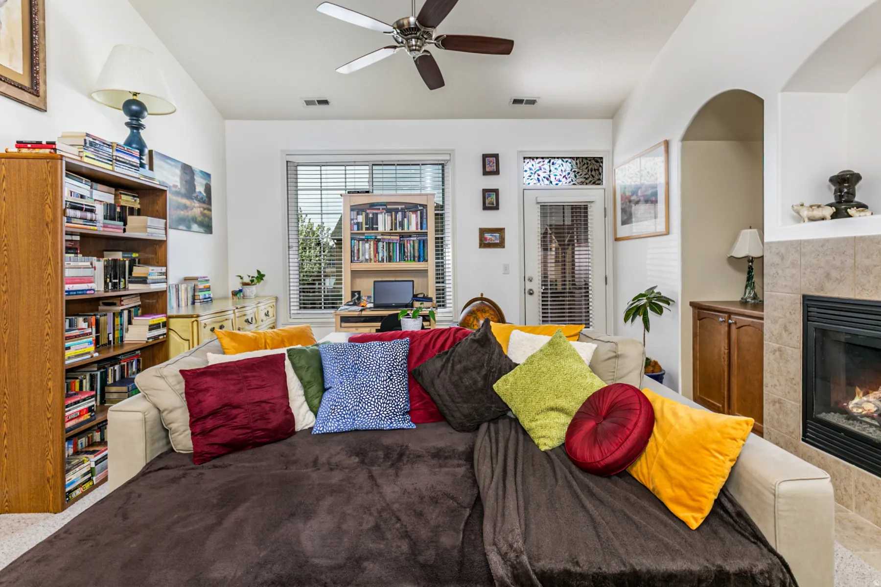 Carpeted living area featuring a tiled fireplace, a ceiling fan, and lofted ceiling