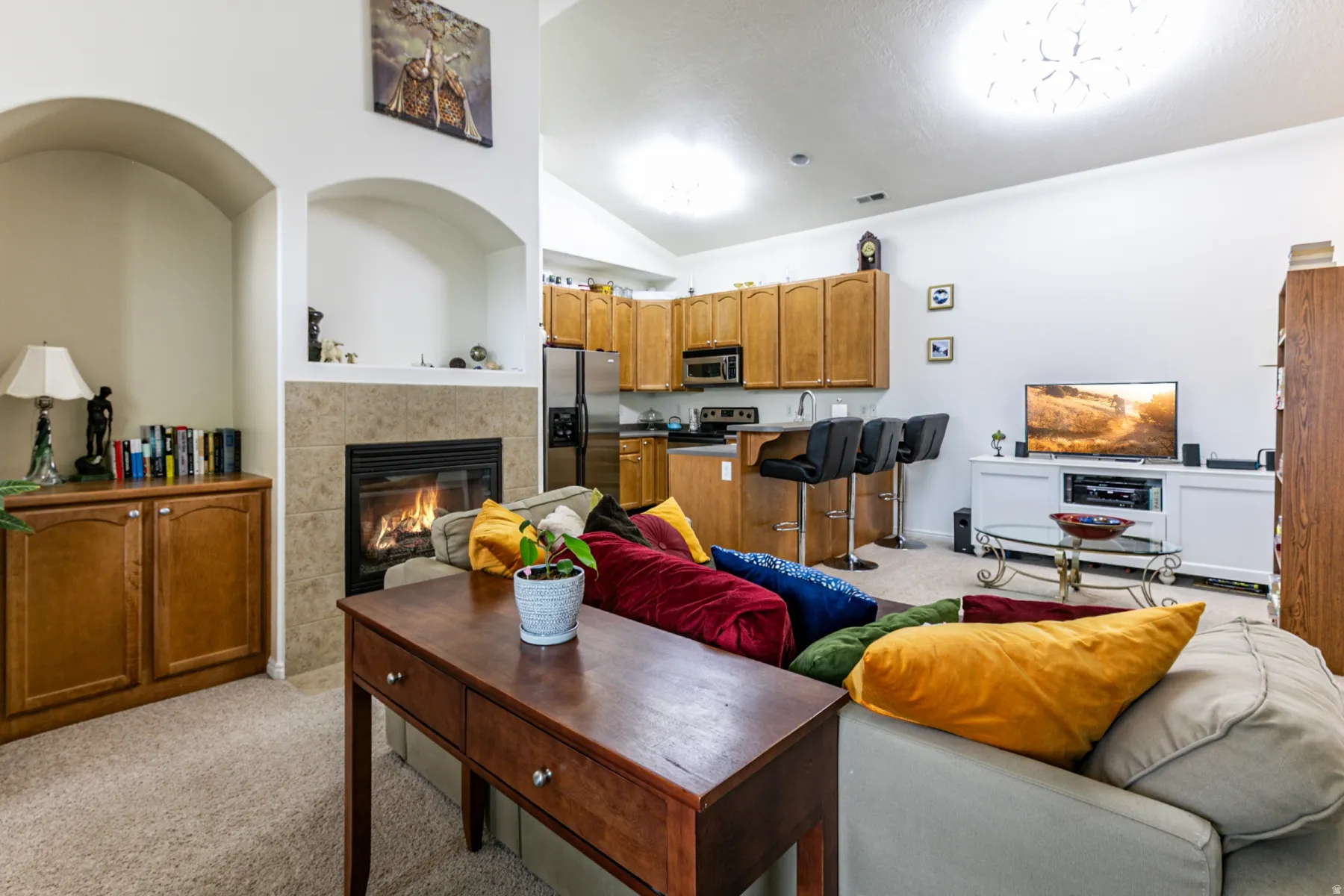 Living area with light colored carpet, a tile fireplace, and vaulted ceiling