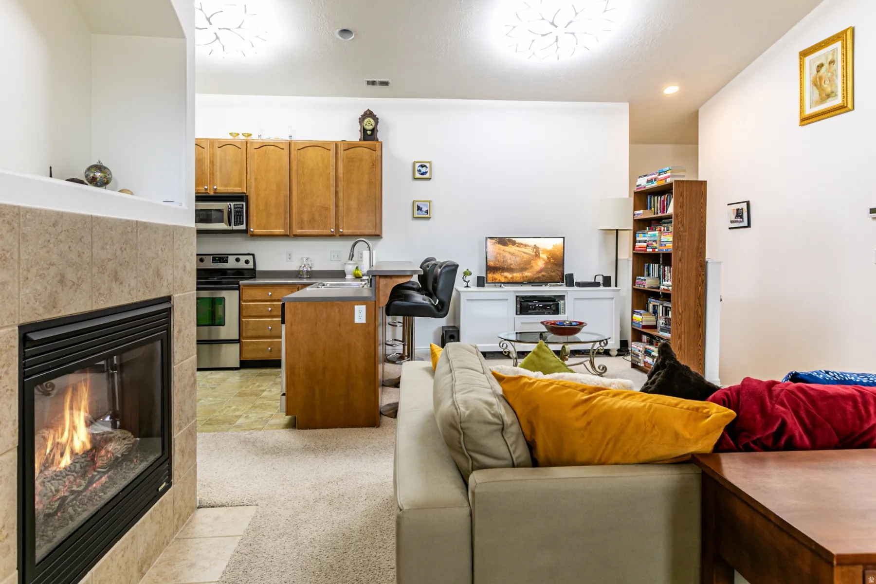 Kitchen with open floor plan, a tiled fireplace, wood finish cabinetry, stainless steel appliances, and dark countertops