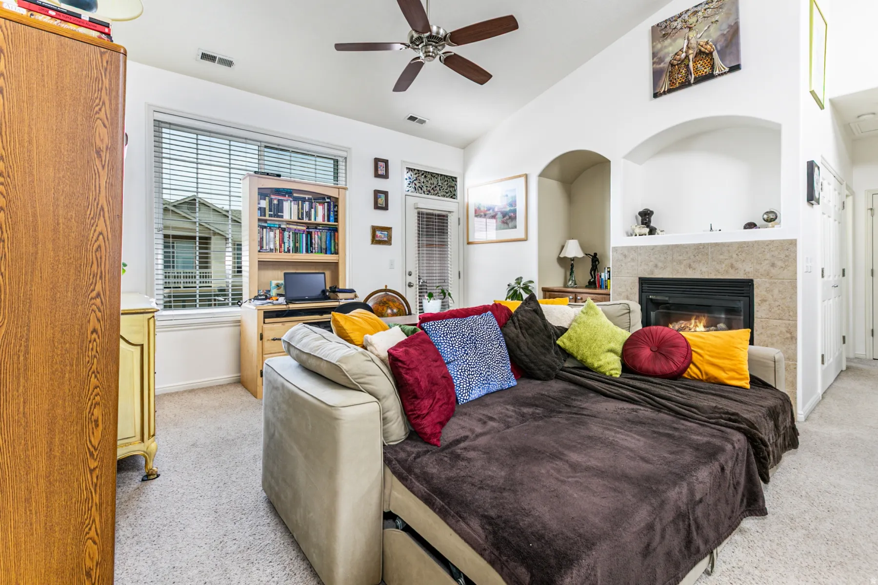 Living area featuring light carpet, vaulted ceiling, a tiled fireplace, and ceiling fan