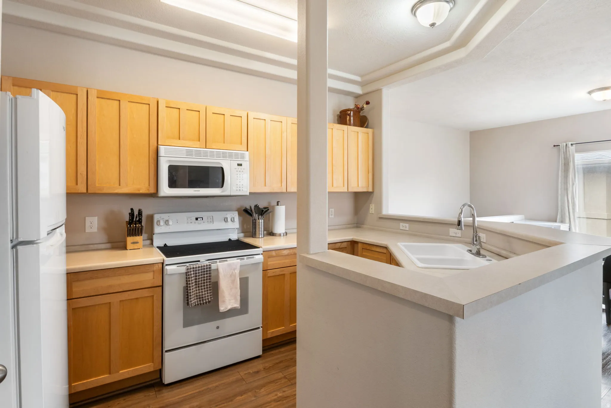 Kitchen featuring white appliances, light countertops, light wood finish cabinetry, dark wood-style floors, and a raised ceiling