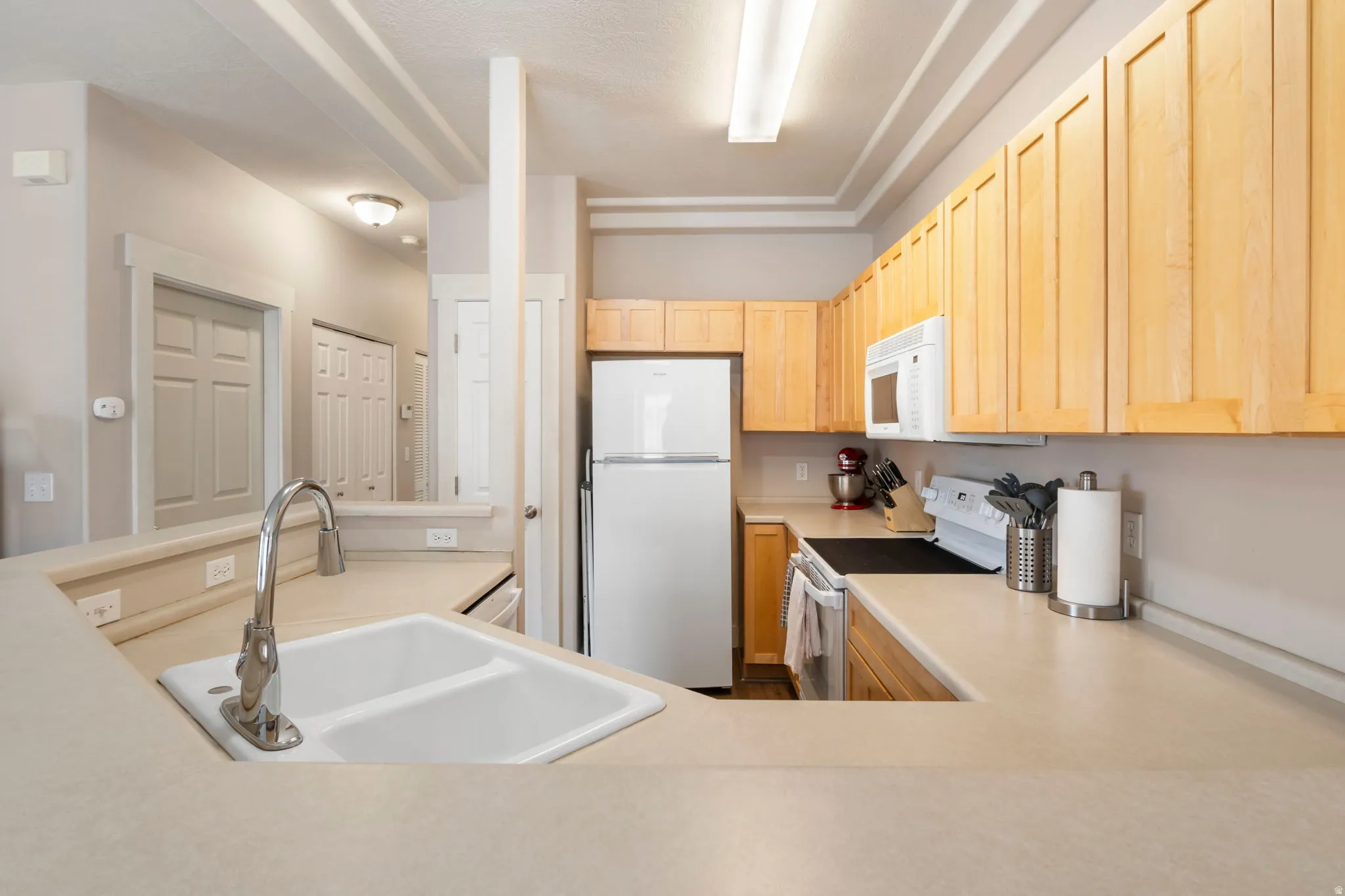 Kitchen with white appliances, light countertops, light wood finish cabinets, and a peninsula