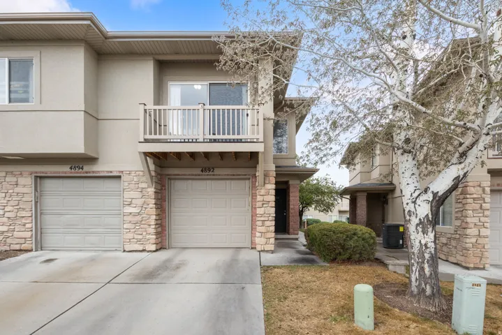 View of front facade with an attached garage, a balcony, stucco siding, stone siding, and driveway