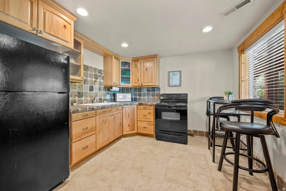 Kitchen with black appliances, glass fronted cabinets, light wood finish cabinetry, and recessed lighting