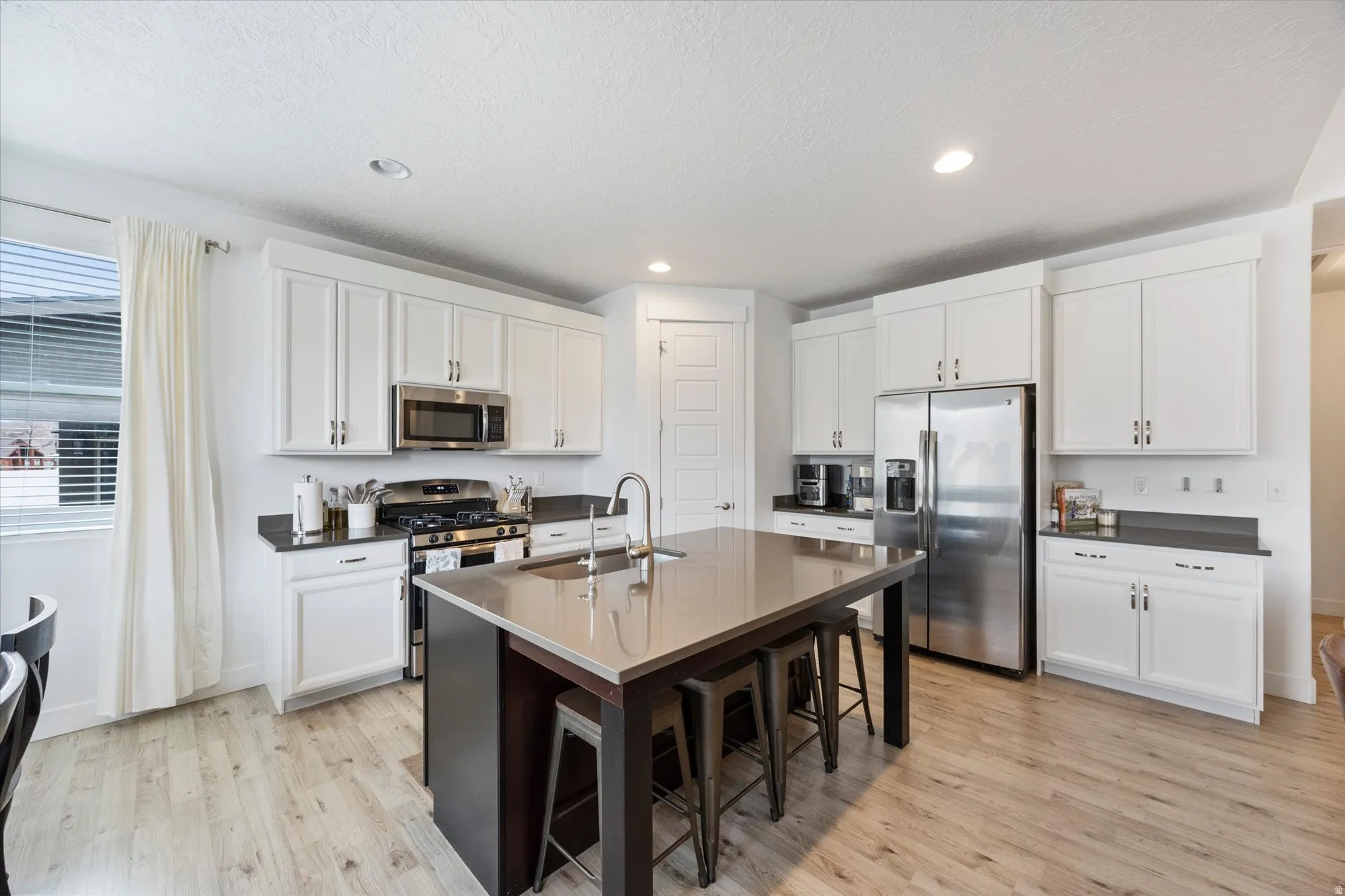 Dual tone kitchen featuring stainless steel appliances, a breakfast bar area, light wood-type flooring, an island with sink, and recessed lighting
