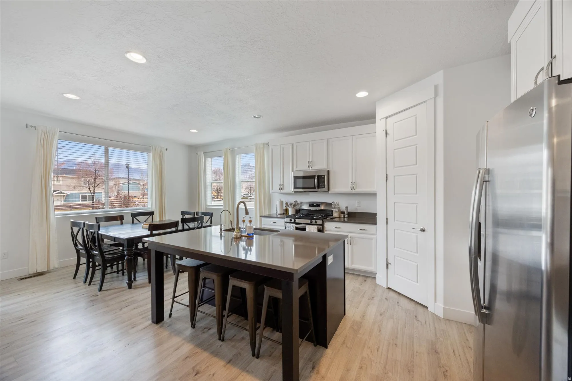 Dual tone kitchen with stainless steel appliances, a center island with sink, light wood-type flooring, a breakfast bar, and a textured ceiling