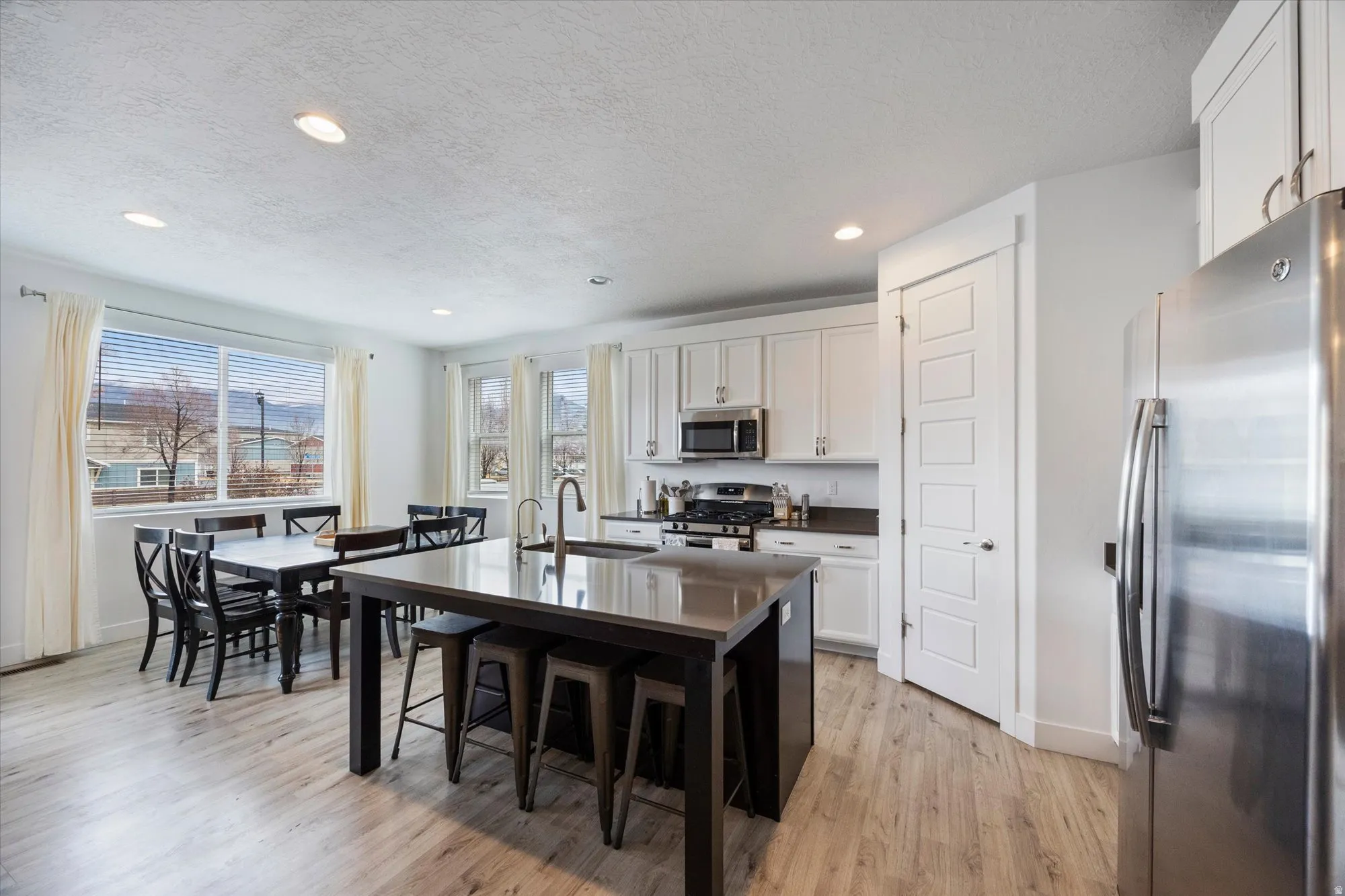 Kitchen with stainless steel appliances, white cabinets, light wood-style flooring, a textured ceiling, and a breakfast bar area
