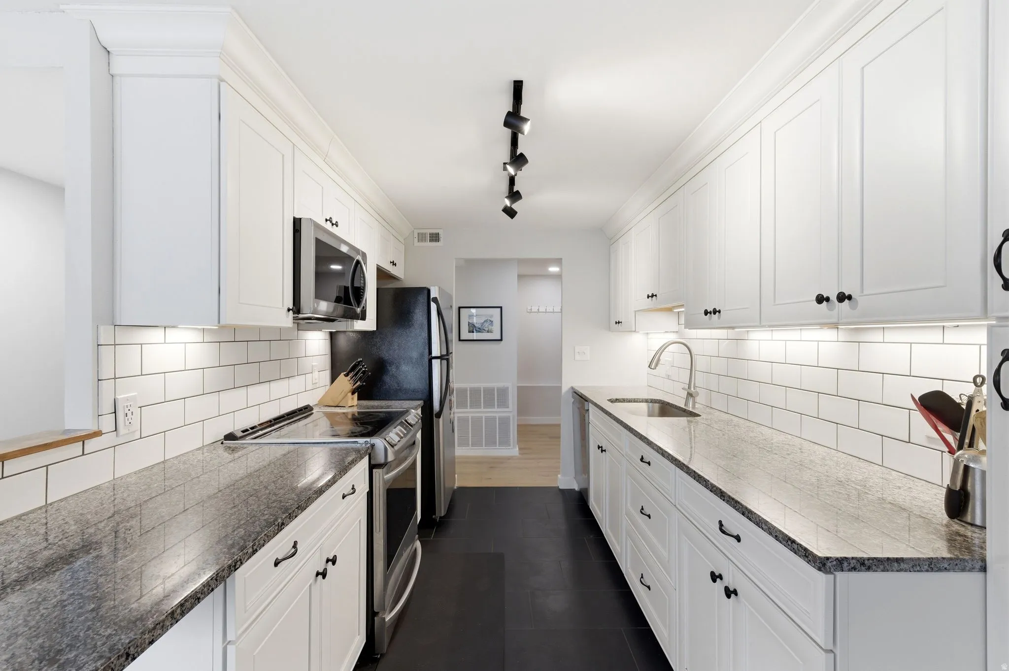 Kitchen with stainless steel appliances, white cabinets, track lighting, dark stone countertops, and dark slate tile patterned floors